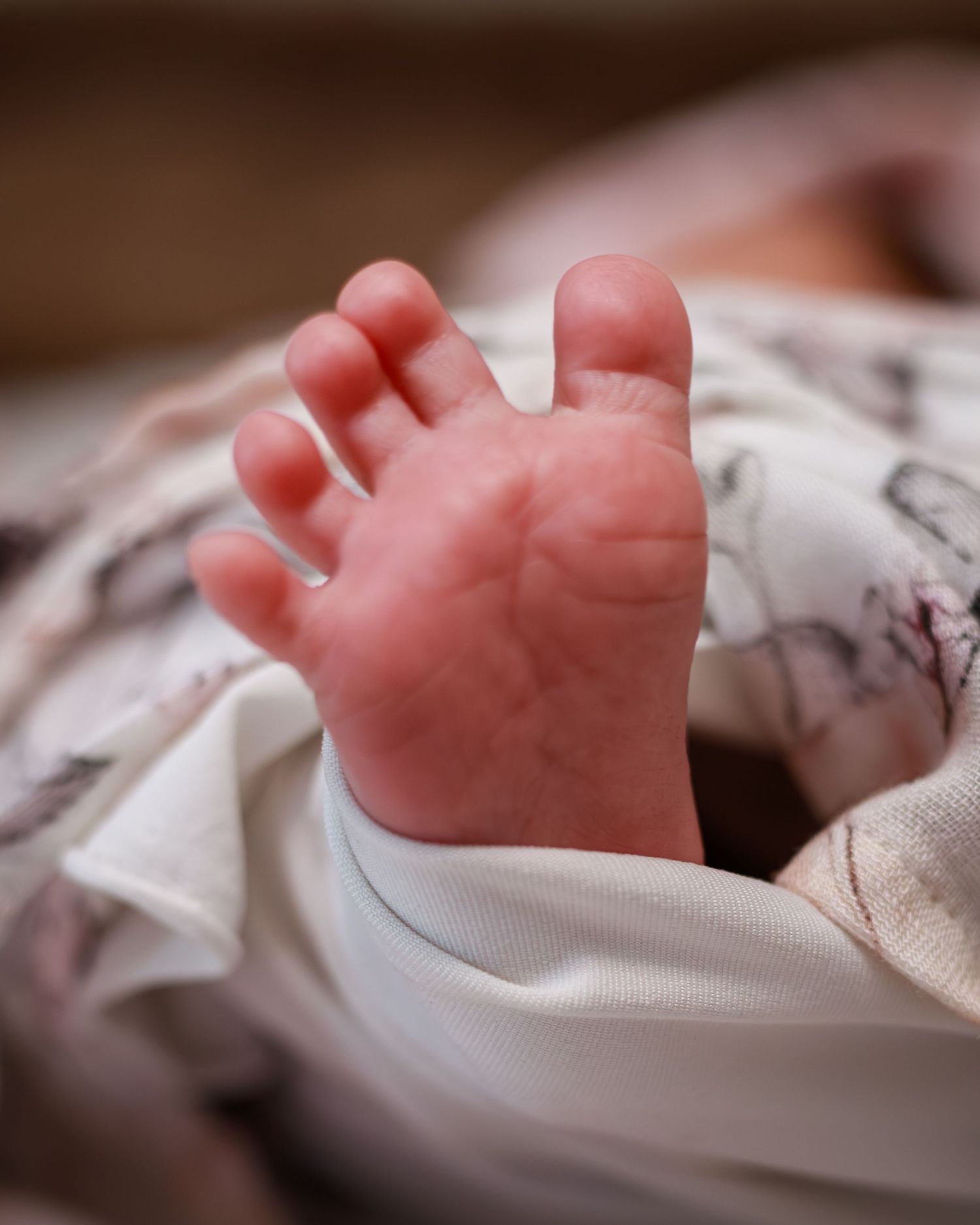 Close-up of a newborn baby's tiny foot peeking out from a soft white swaddle blanket.