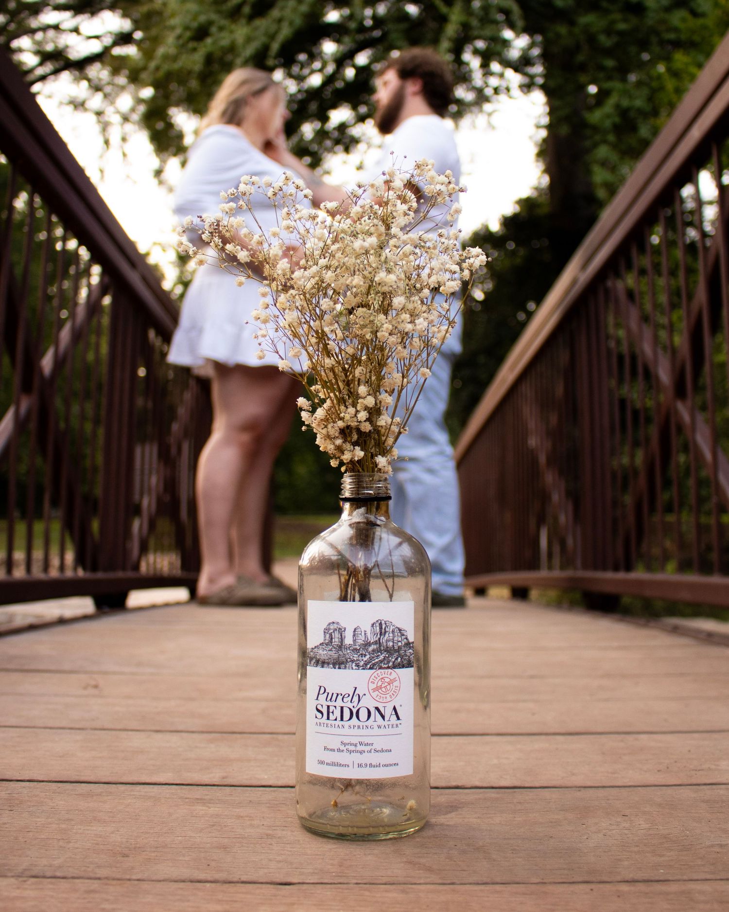 Mason jars with dried flowers sit on a wooden bridge during a rustic outdoor photoshoot.