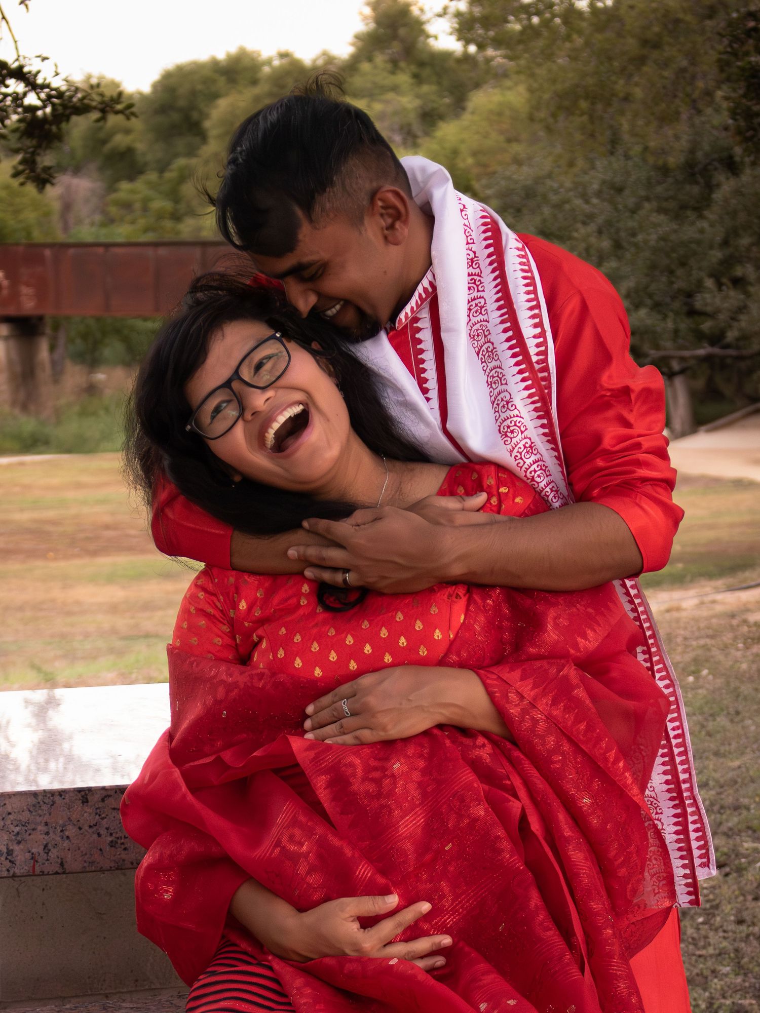 Couple wearing red outfits embrace and laugh together during their outdoor portrait session.