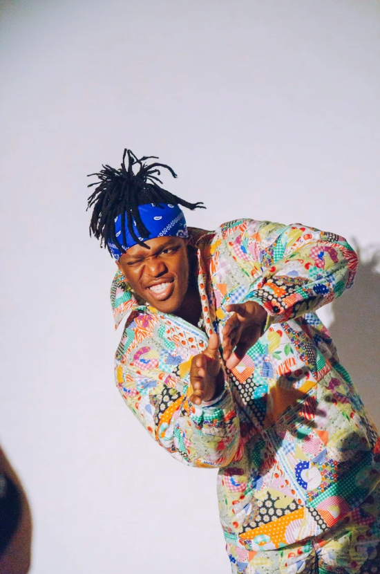 Person in colorful patterned outfit posing playfully against white background.