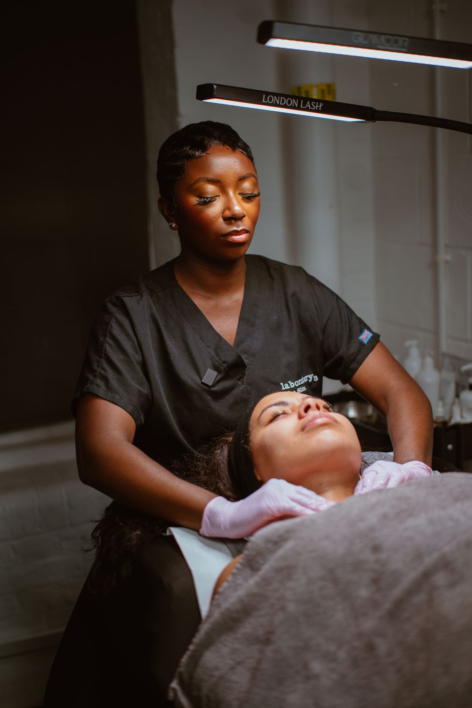 Spa professional performing a facial treatment on a client in a dimly lit room.