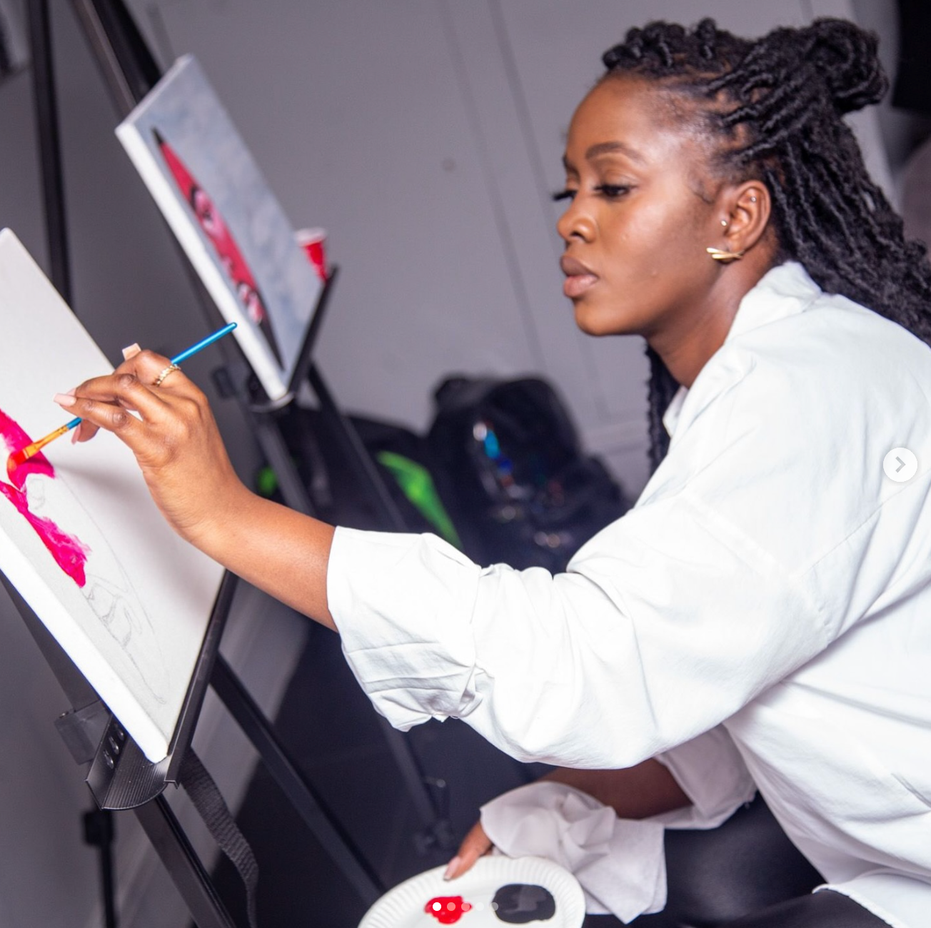 Artist in white attire focused on creating artwork at an easel.
