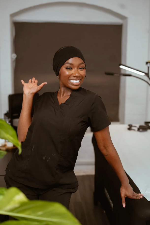Person in black uniform and head covering smiles while working in a professional setting.