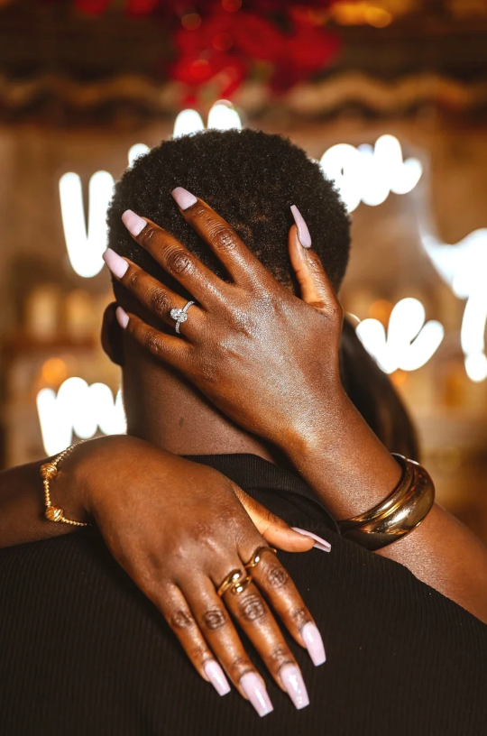 Close-up of manicured hands with rings against dark background with bokeh lights.