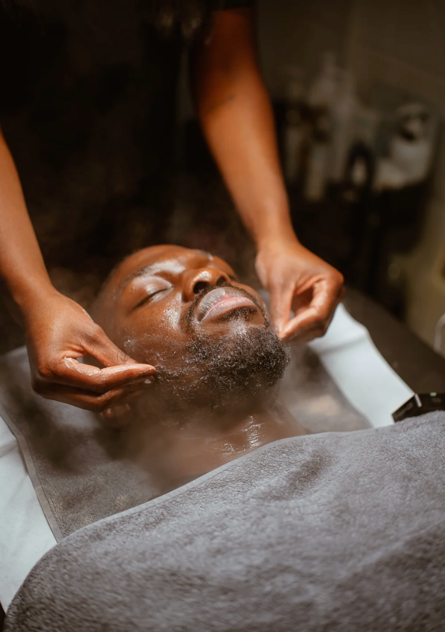 Close-up of spa facial treatment with hands massaging client's face on gray towel.