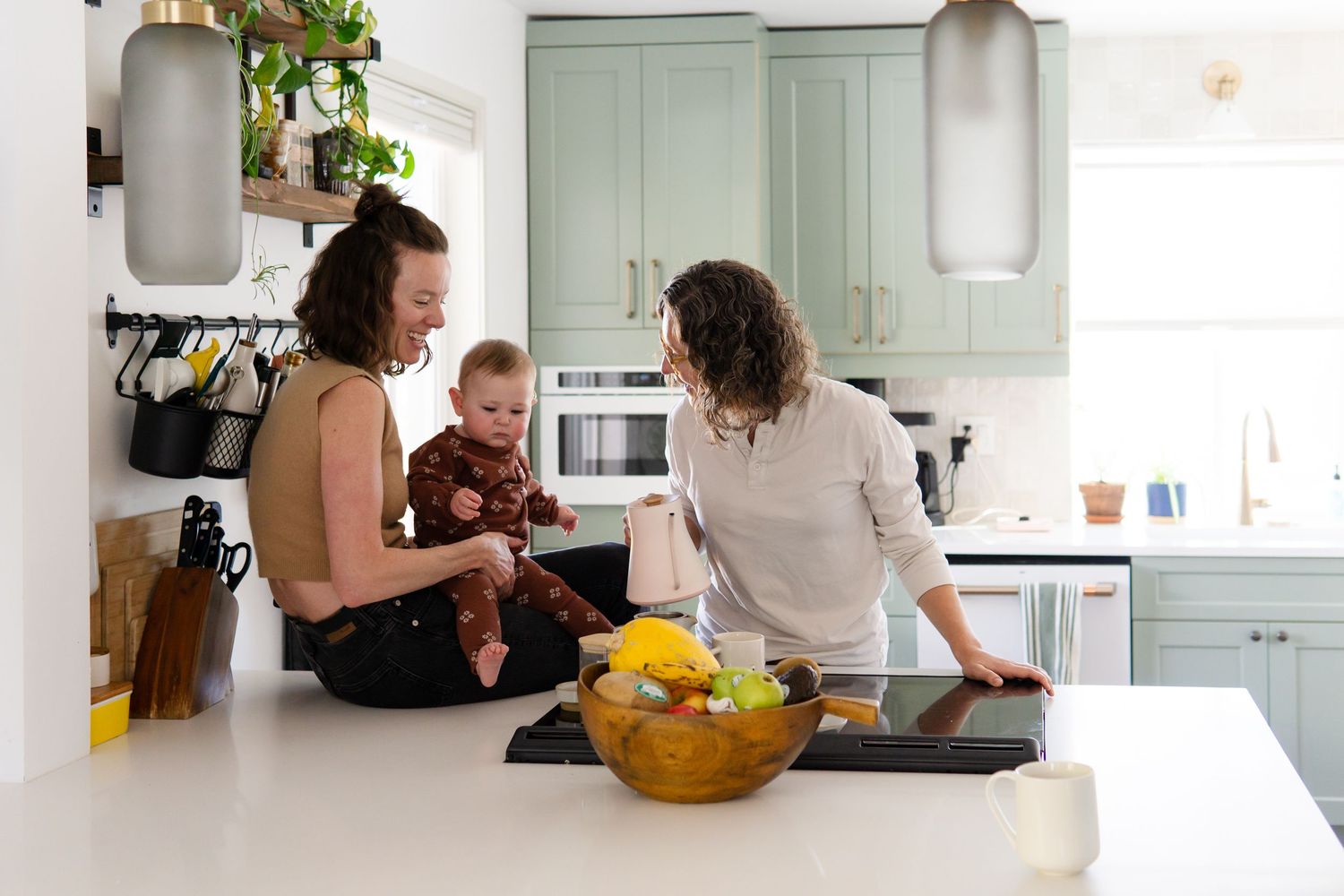 Candid lifestyle photography session showing people interacting in a bright modern kitchen with white cabinets.