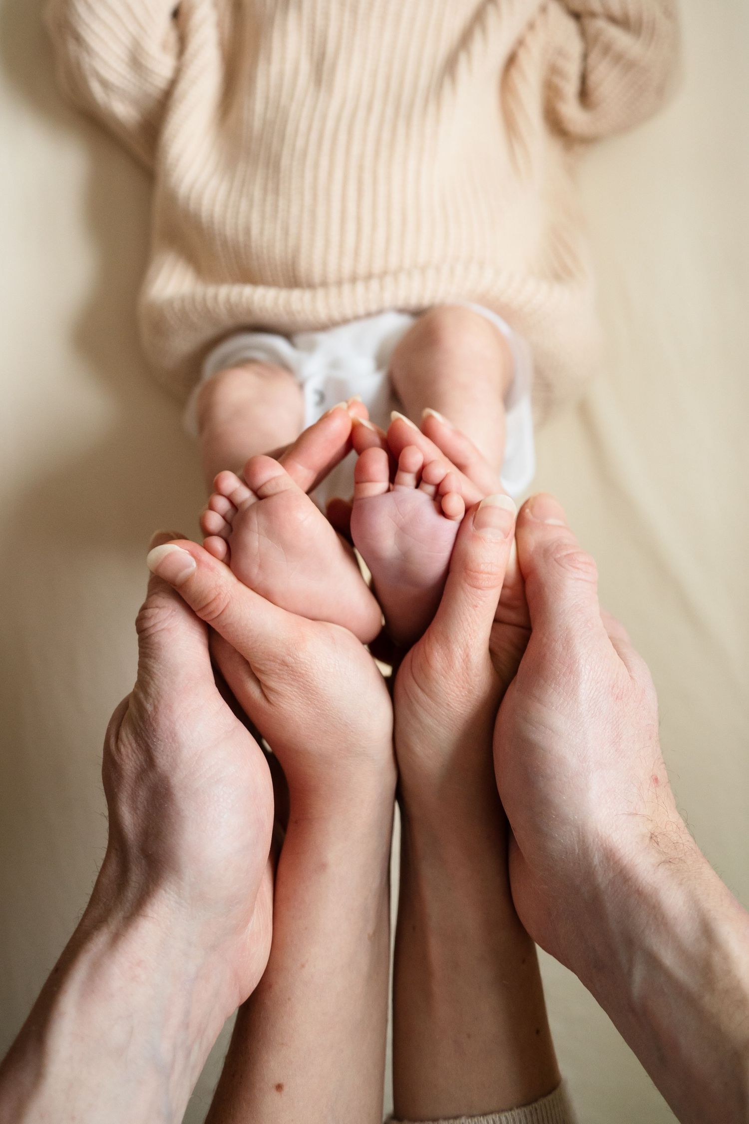 Multiple hands gently holding tiny baby feet against a neutral background.