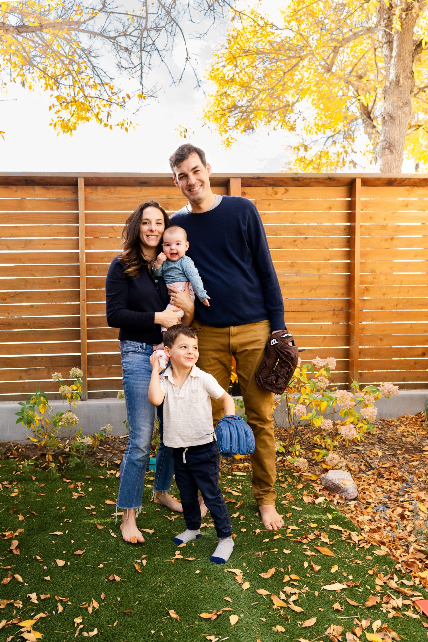 Family enjoying autumn day together in backyard with wooden fence and fallen leaves.