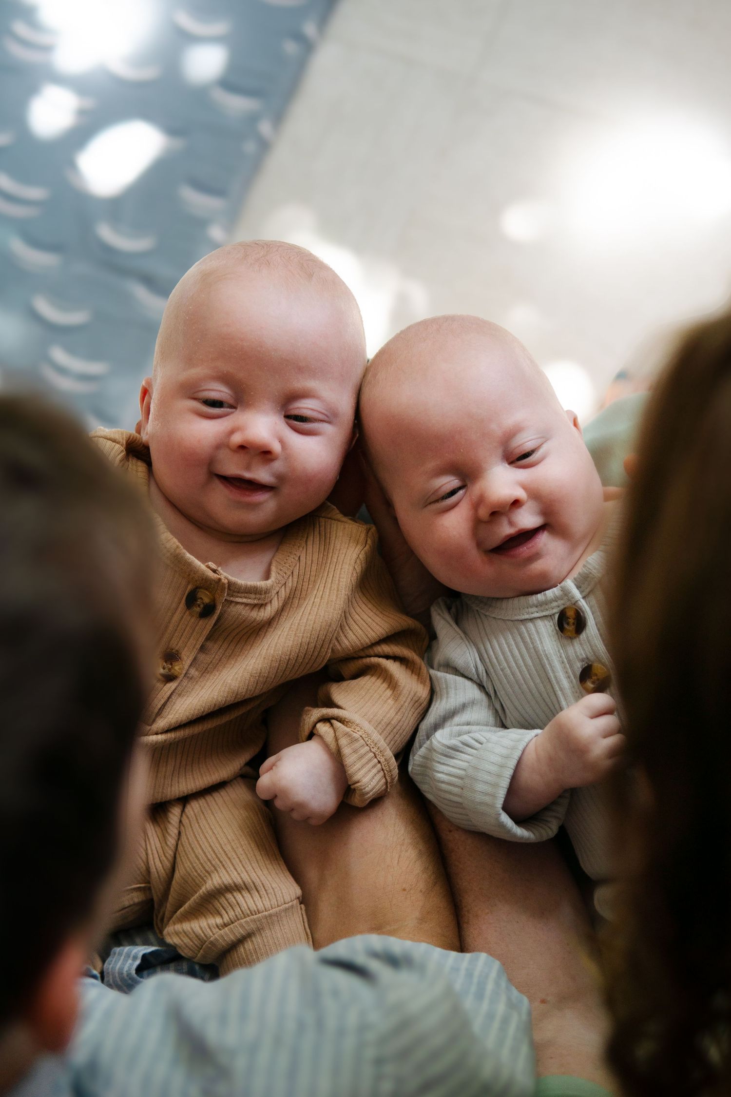 Two babies in knit sweaters laughing together on floor.