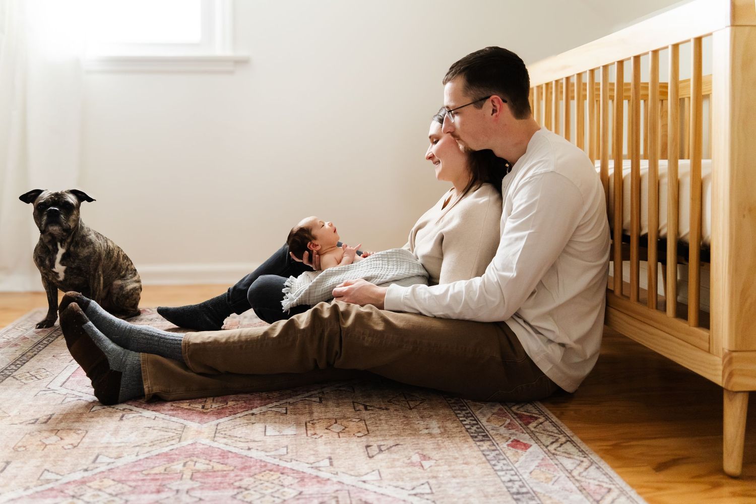 A cozy family scene on hardwood floor with small dog beside wooden crib.