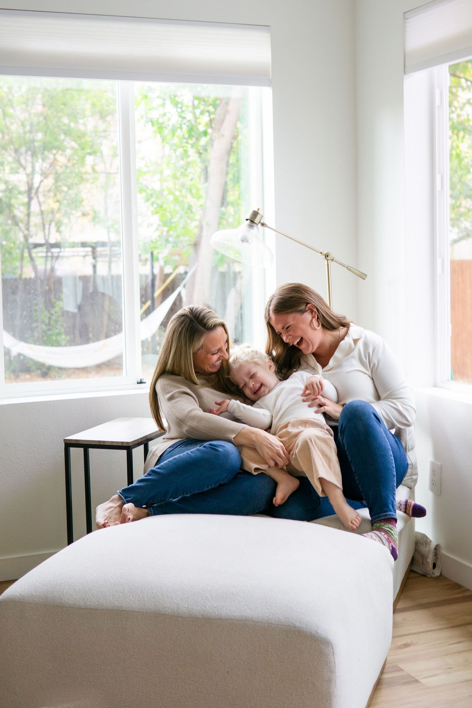 A family sharing a tender moment together on a white couch near a sunny window.