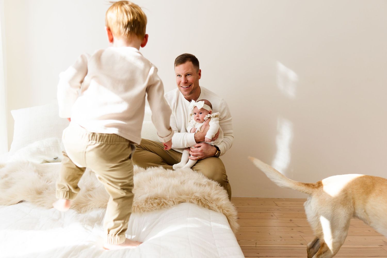 A baby lying on a white blanket in a bright room with natural light streaming in.
