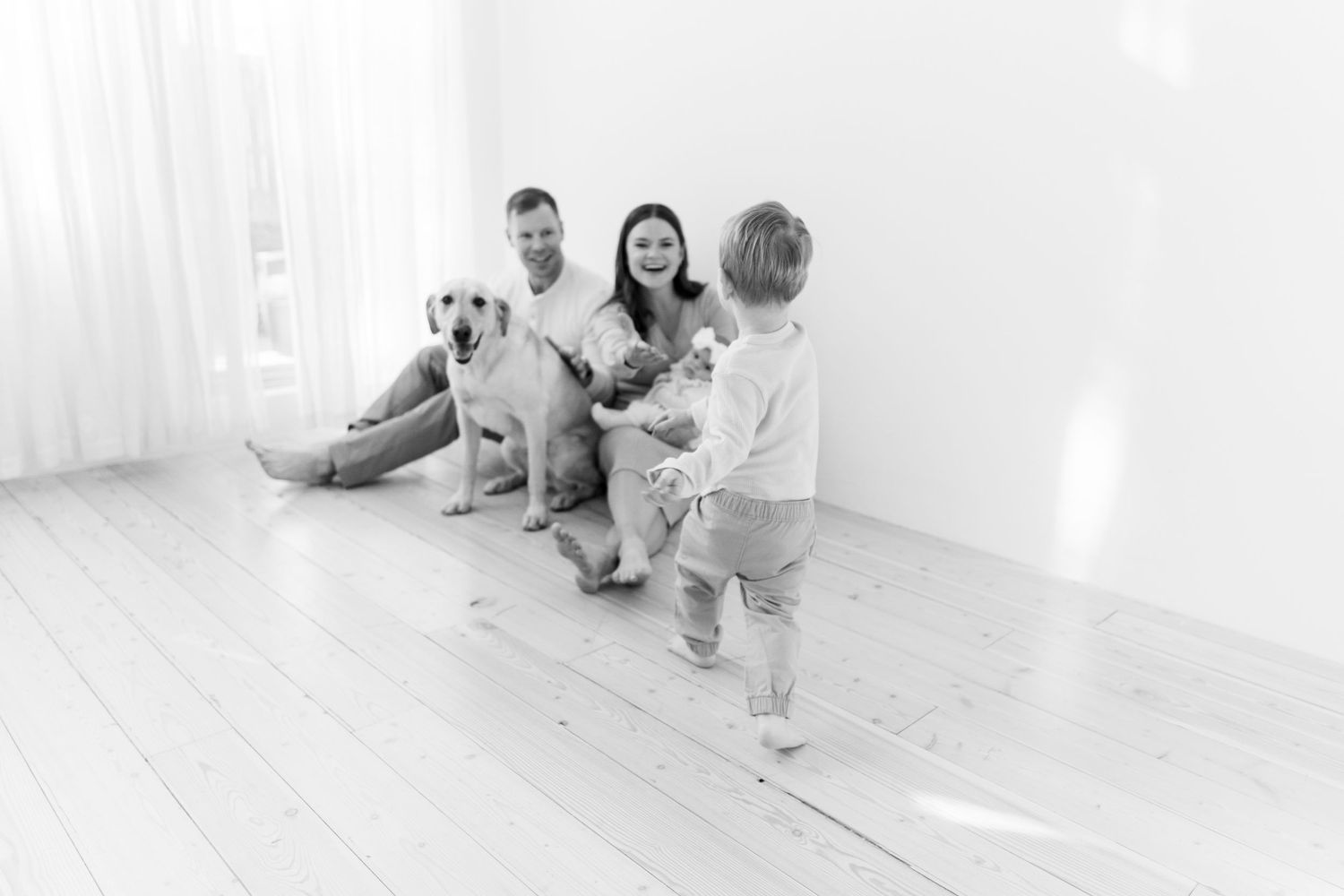Family and pet dog sitting together on white floor for portrait session.
