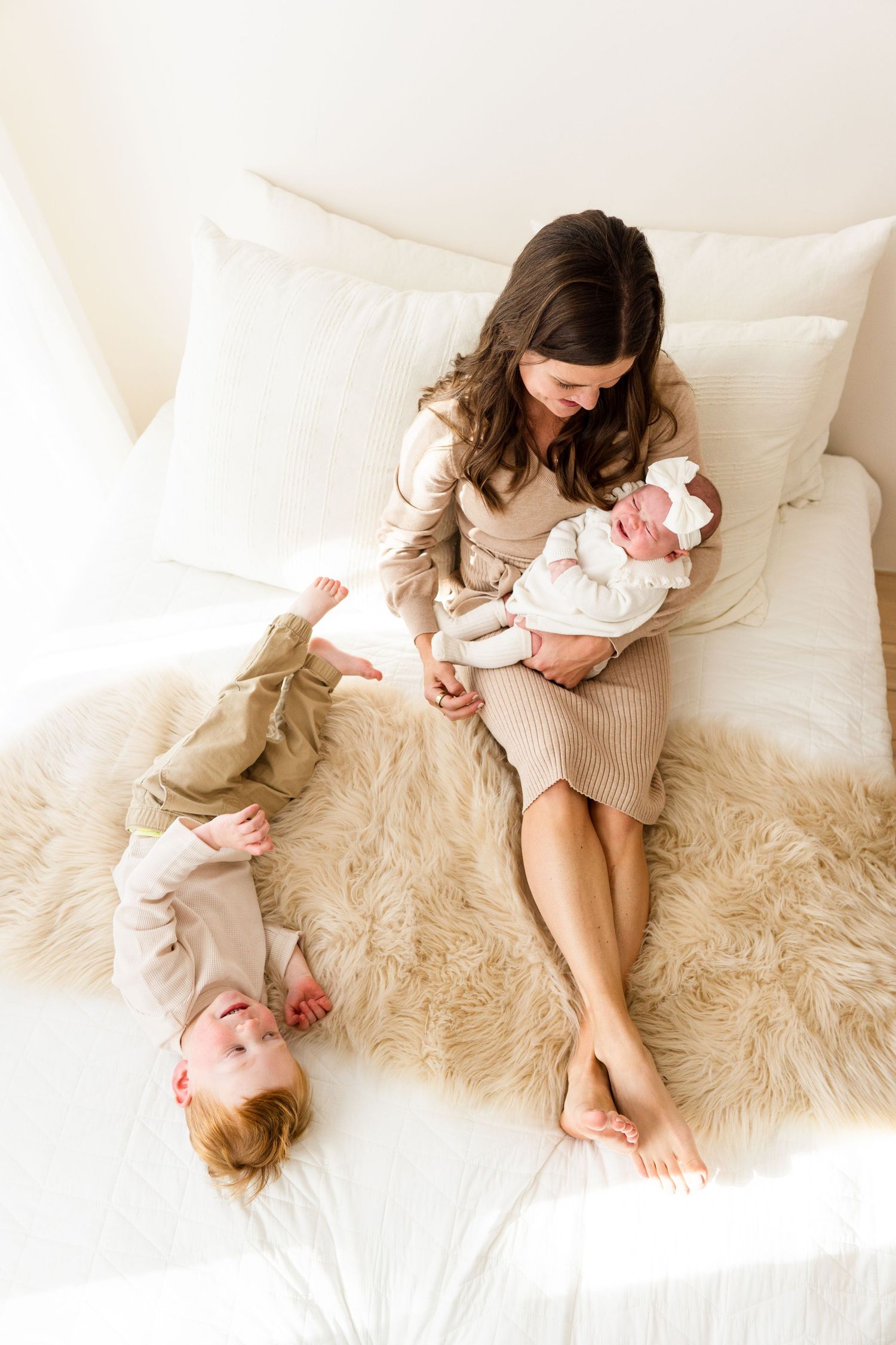 Cozy family moments captured on a plush white bed with fur throw.