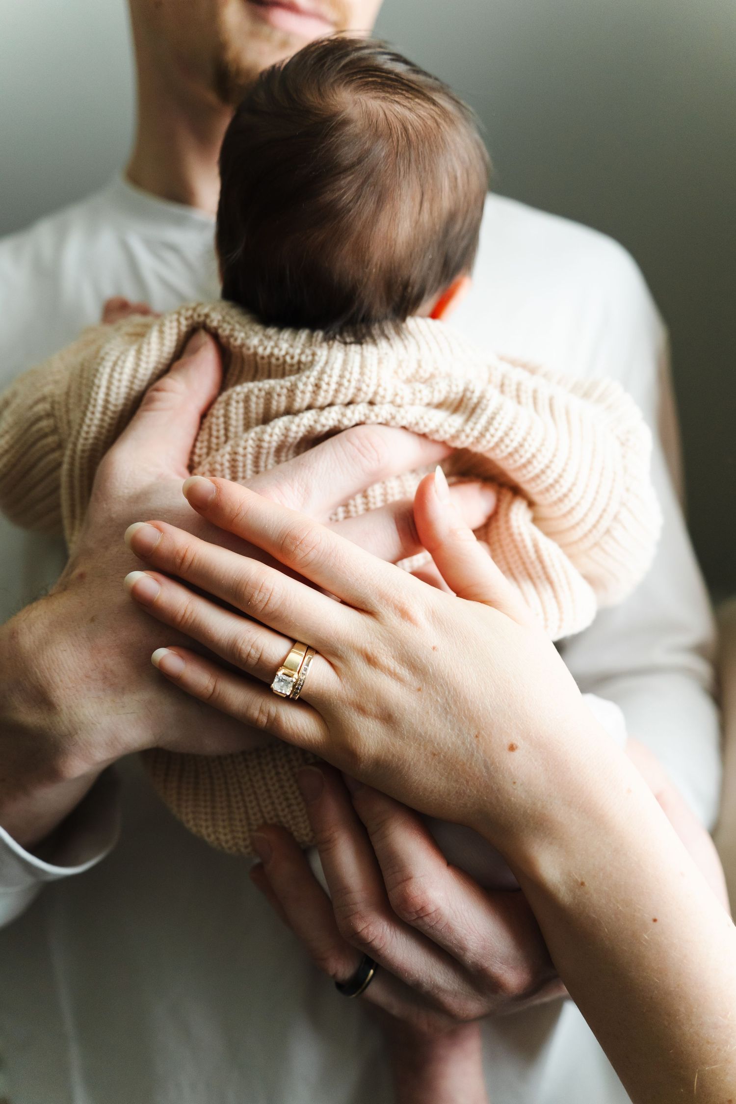 A baby in a knit sweater is held close in loving arms.