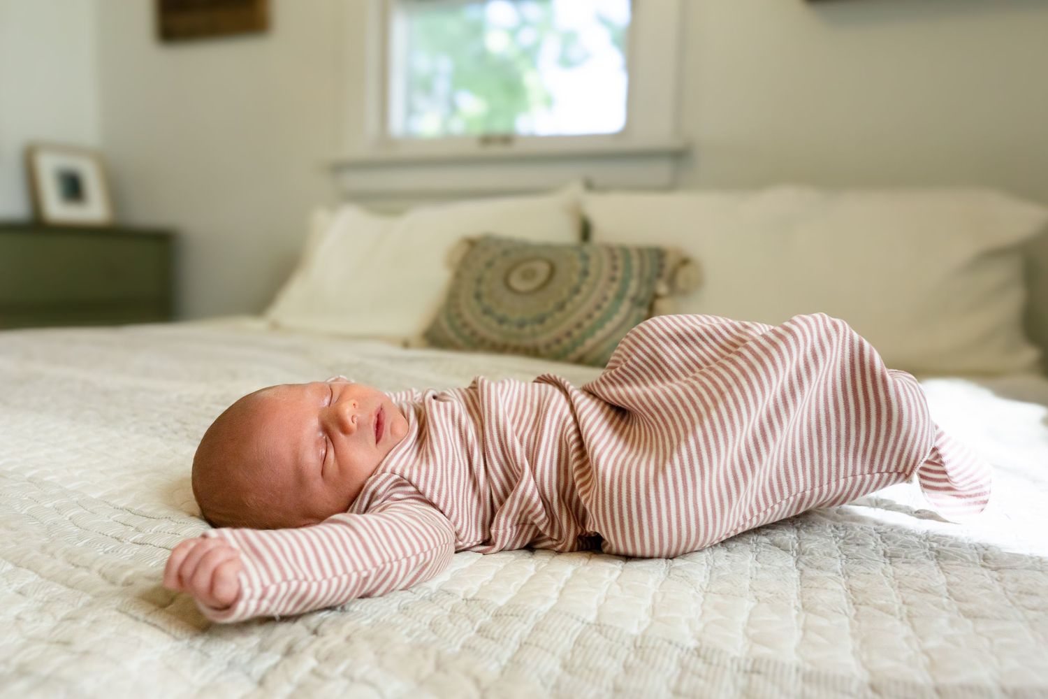 Newborn baby sleeping peacefully on white bedding in natural light.