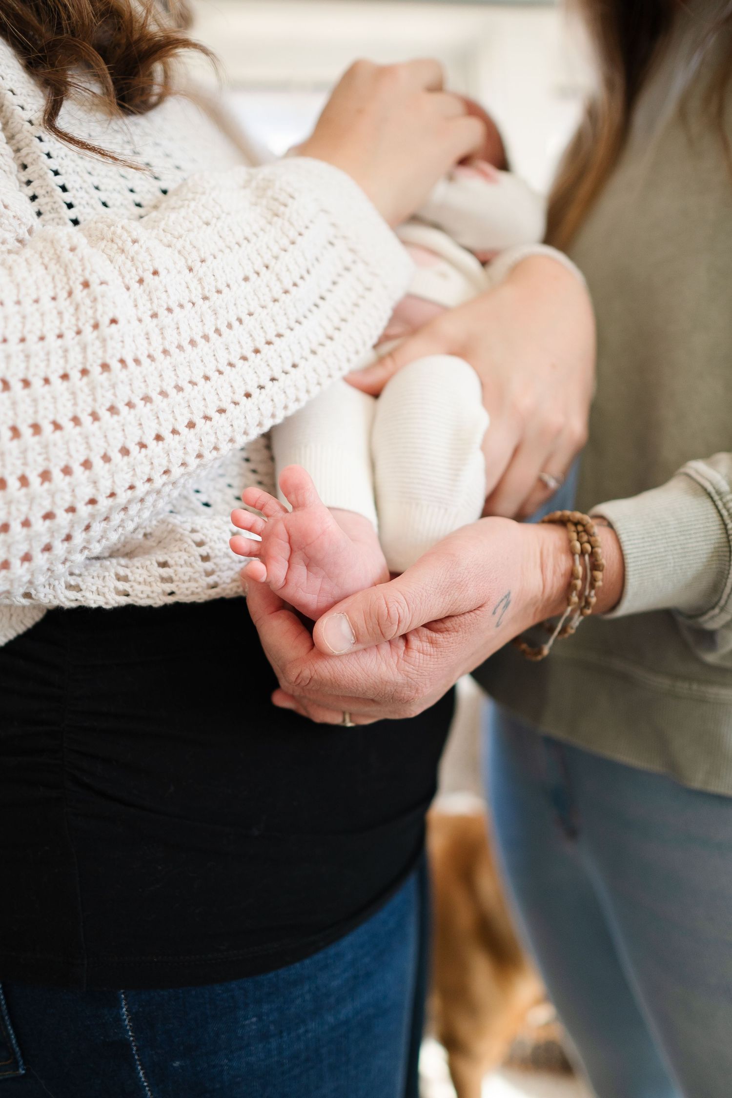 Close-up of gentle hands holding tiny baby feet while wearing a cream knit sweater.