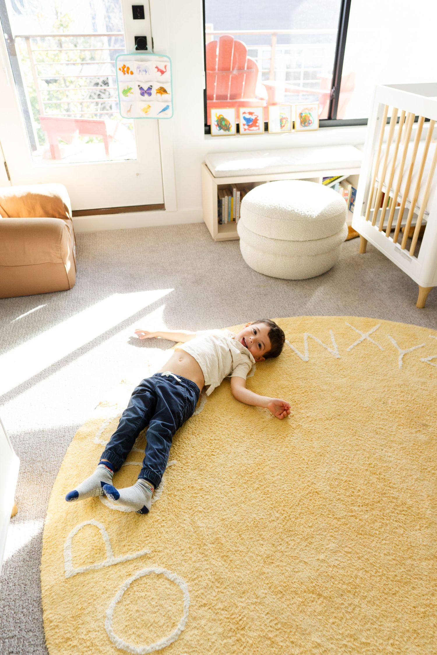 Child playing on a yellow carpet in a sunlit room with educational posters on the wall.