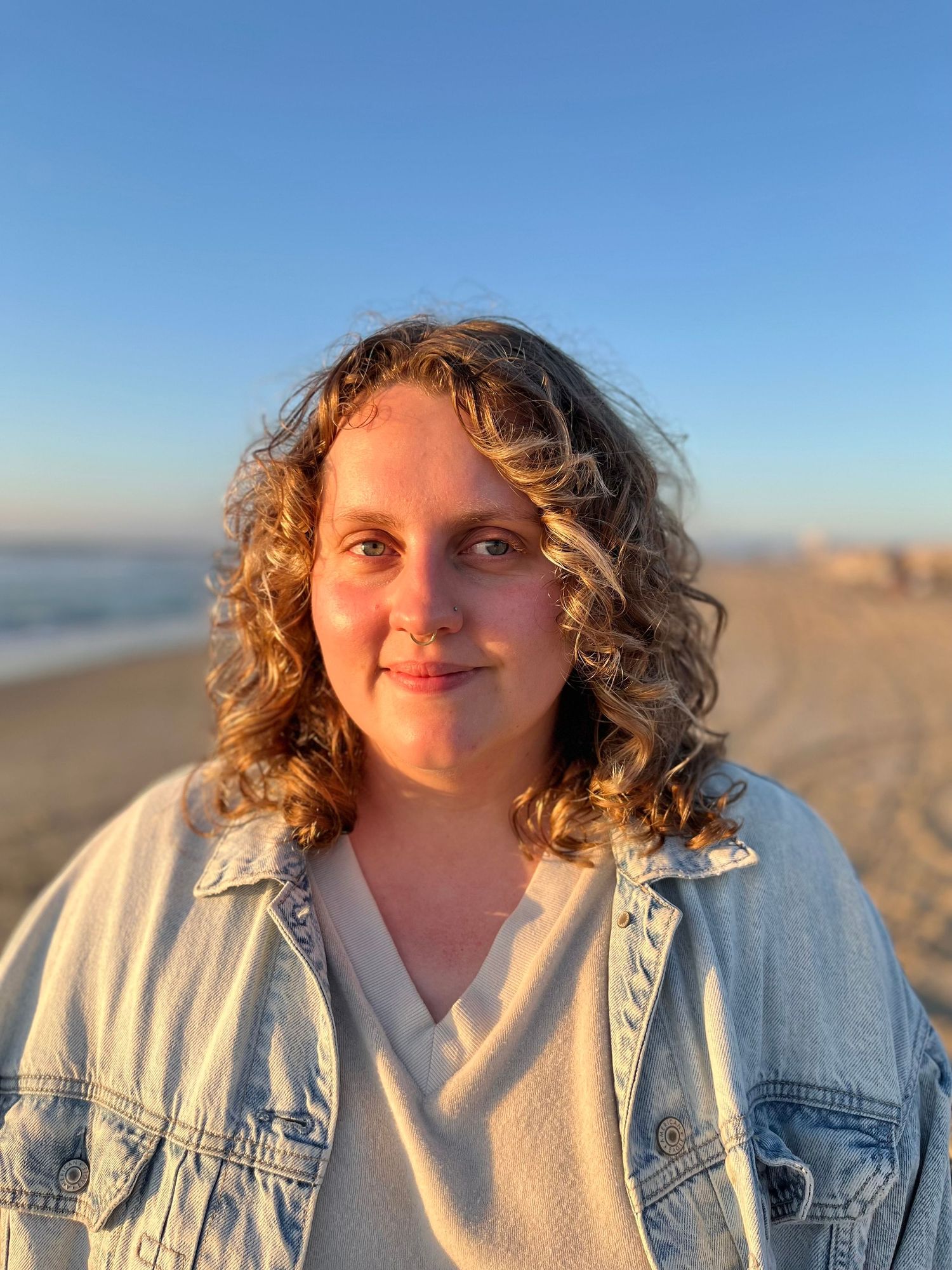 A coastal portrait with natural curls and denim jacket against ocean backdrop.
