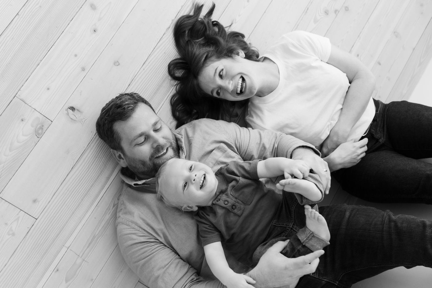 Black and white series of relaxed family moments on light wooden flooring.