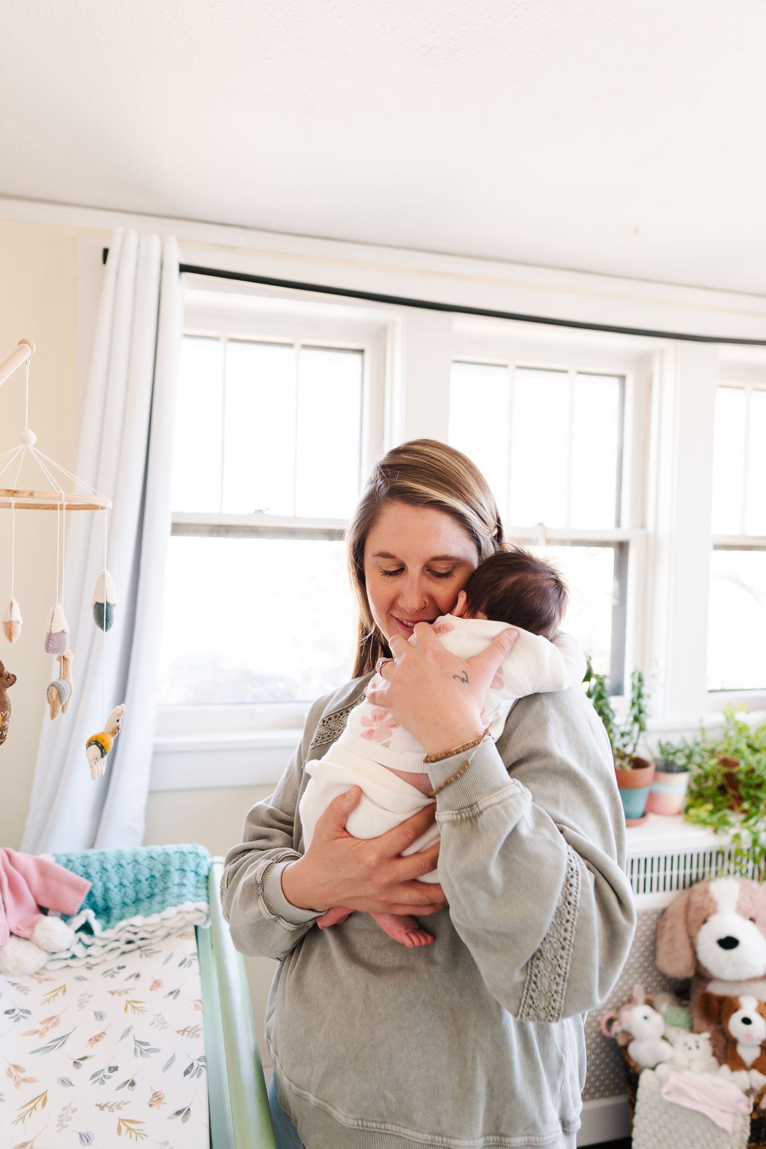 A tender moment in a sunny nursery with floral curtains and stuffed animals.