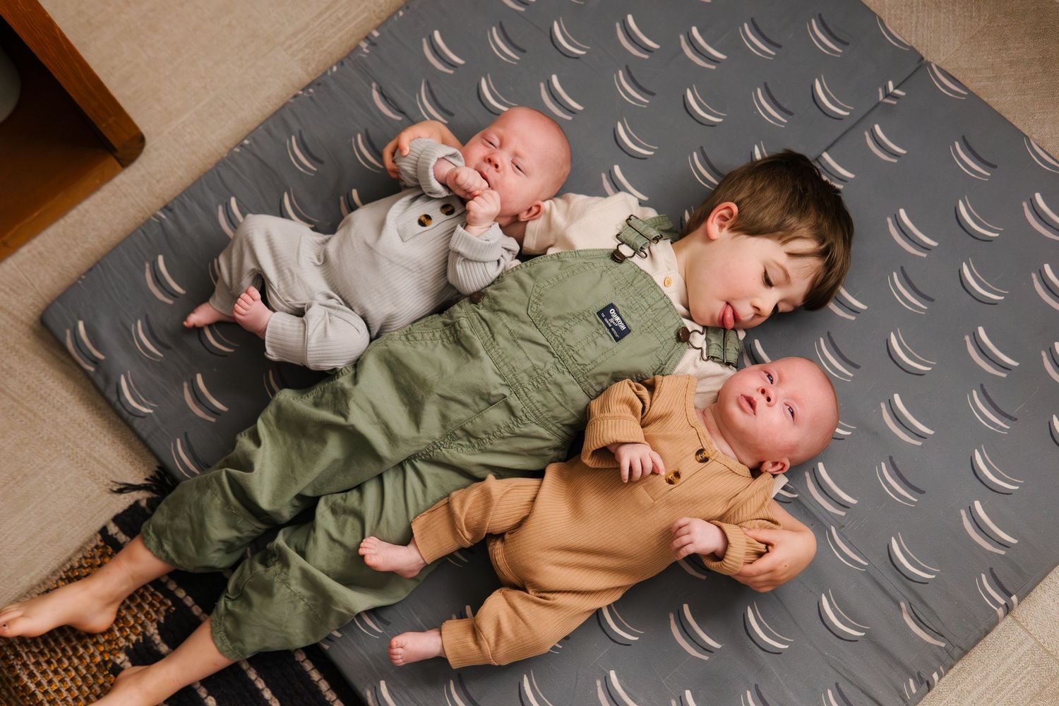 Children relaxing on textured mat in casual clothing.