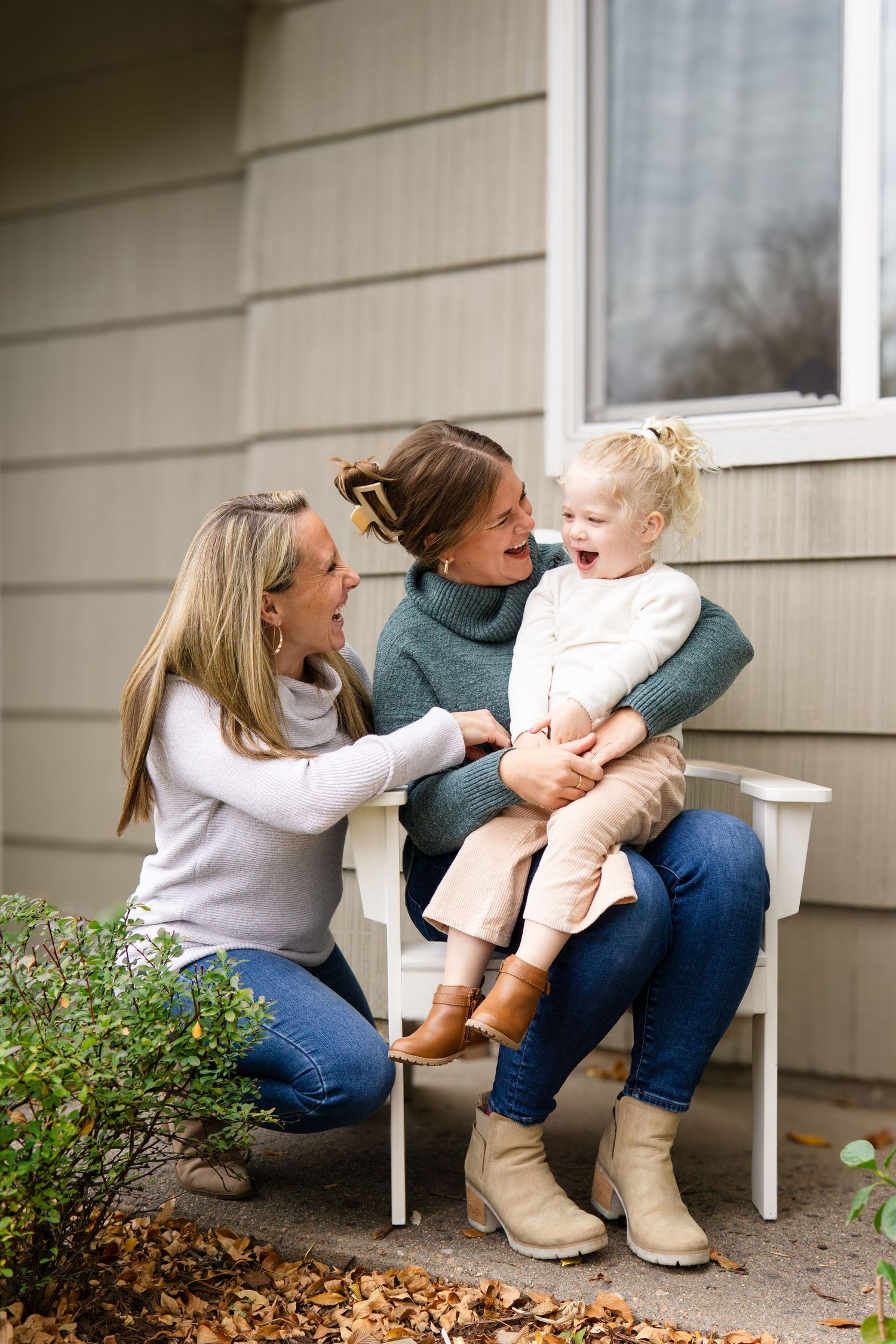 A candid outdoor moment on a white chair against a grey house exterior.