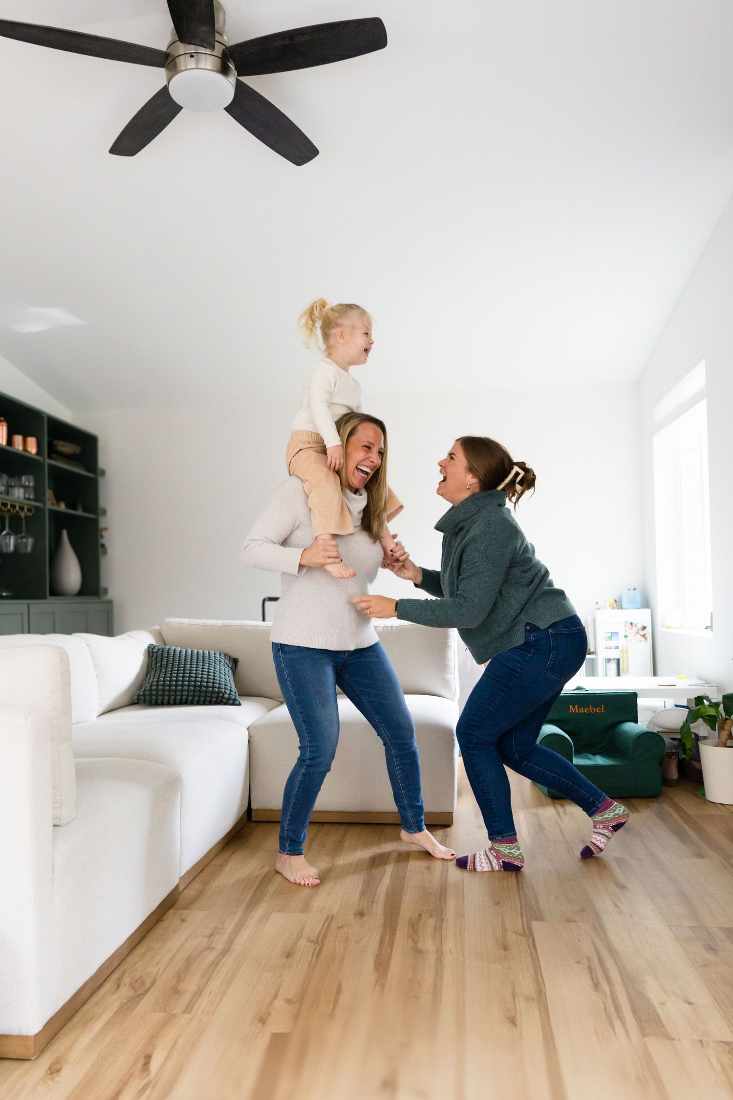 A playful moment in a modern living room with hardwood floors and ceiling fan.