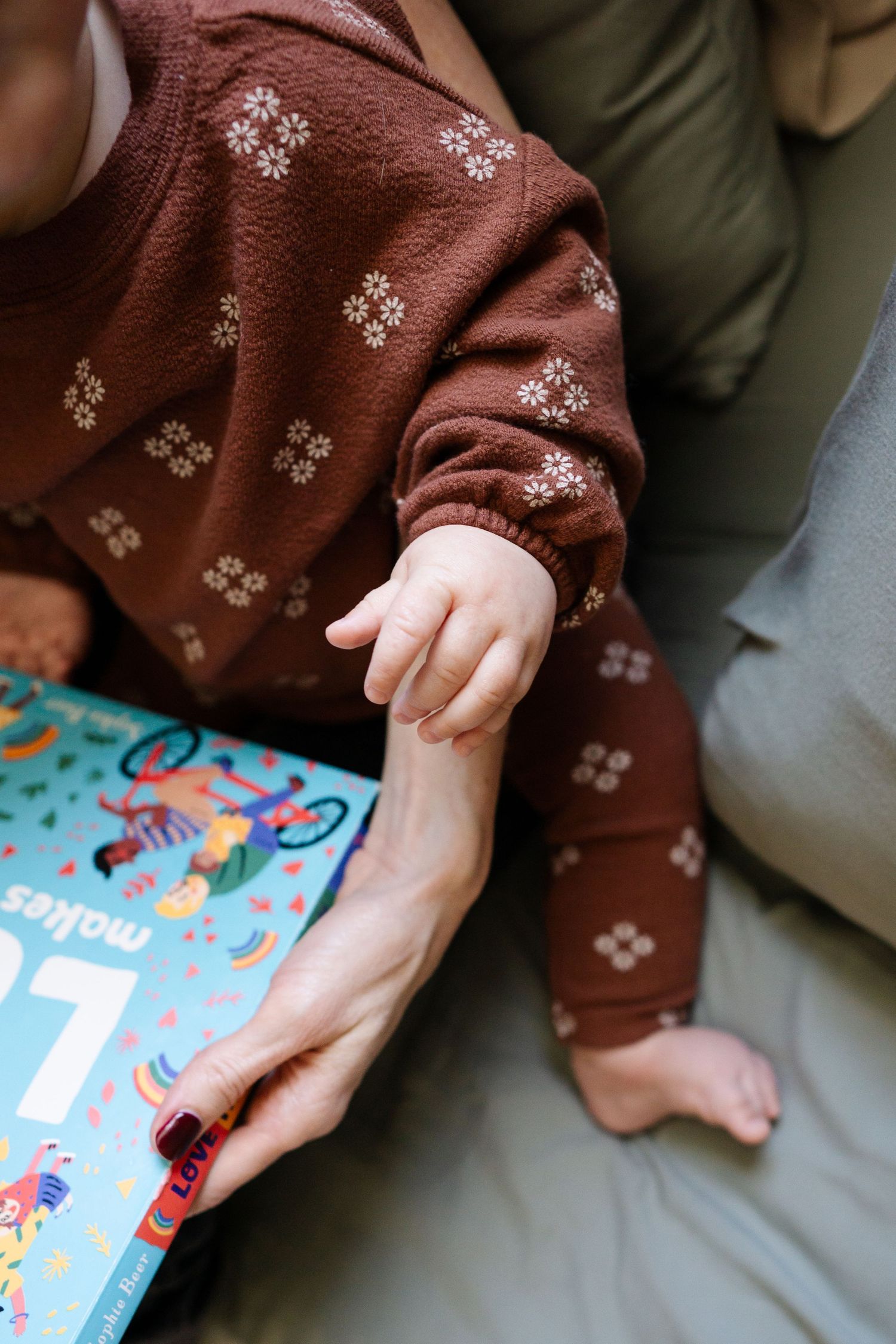 A close-up view of hands holding a children's book with a brown patterned sweater sleeve visible.
