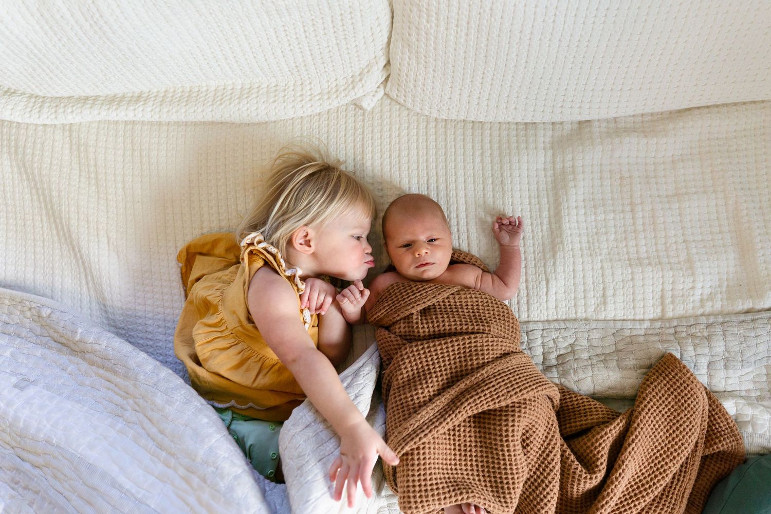 Baby wrapped in brown knit blanket resting on white bedding.