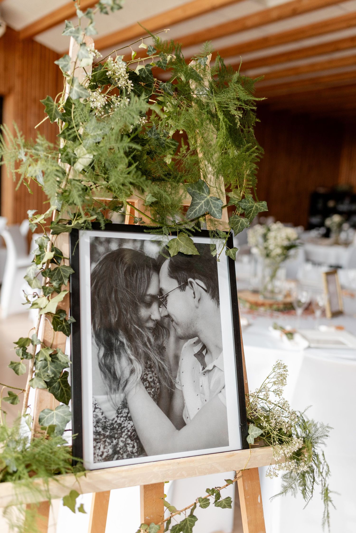 Wedding photo display with black and white portraits hung with greenery decorations.
