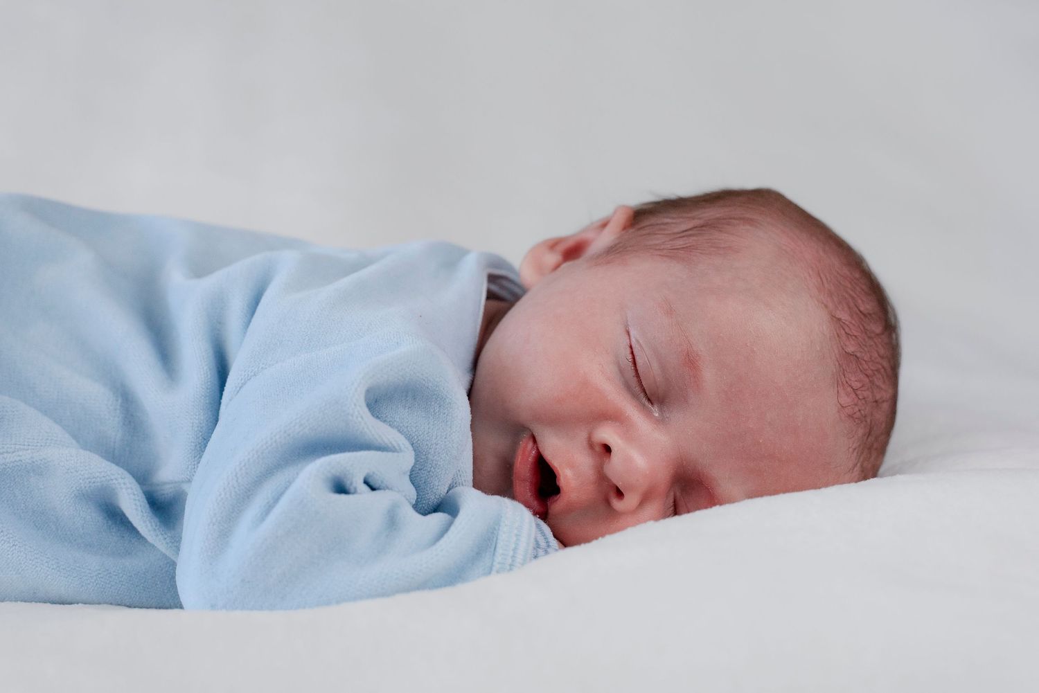 Newborn baby sleeping peacefully wrapped in a soft blue blanket on a white surface.