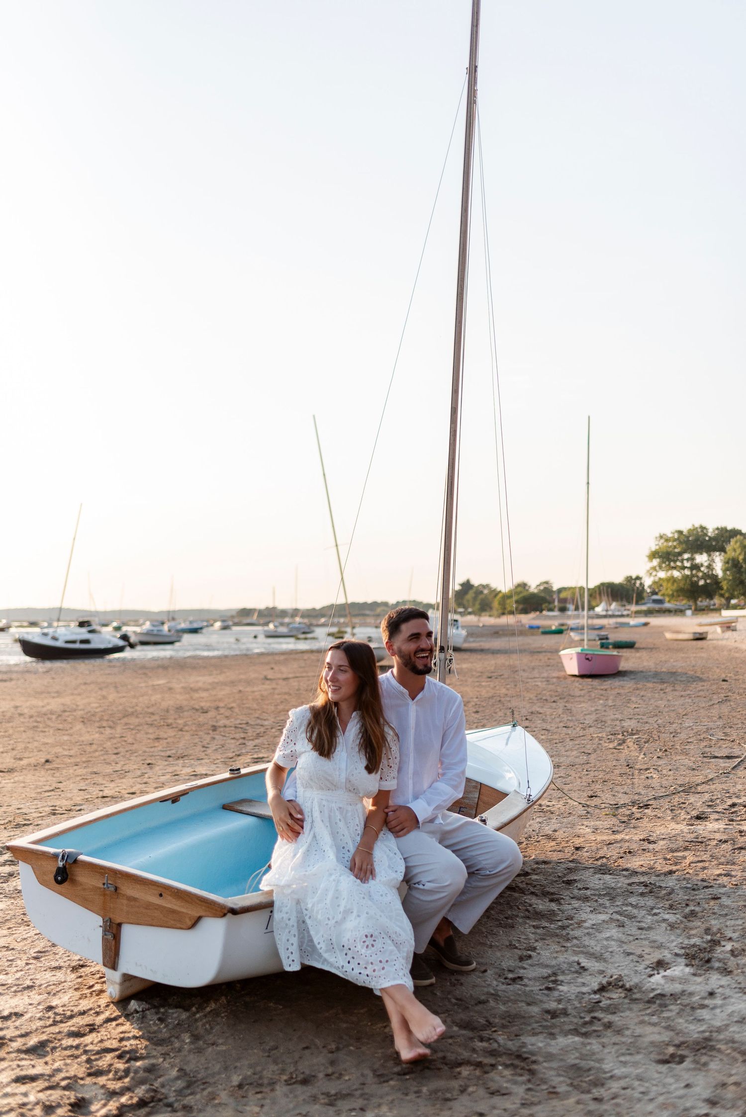 Couple relaxing together in a beached sailboat during a seaside photoshoot at sunset.