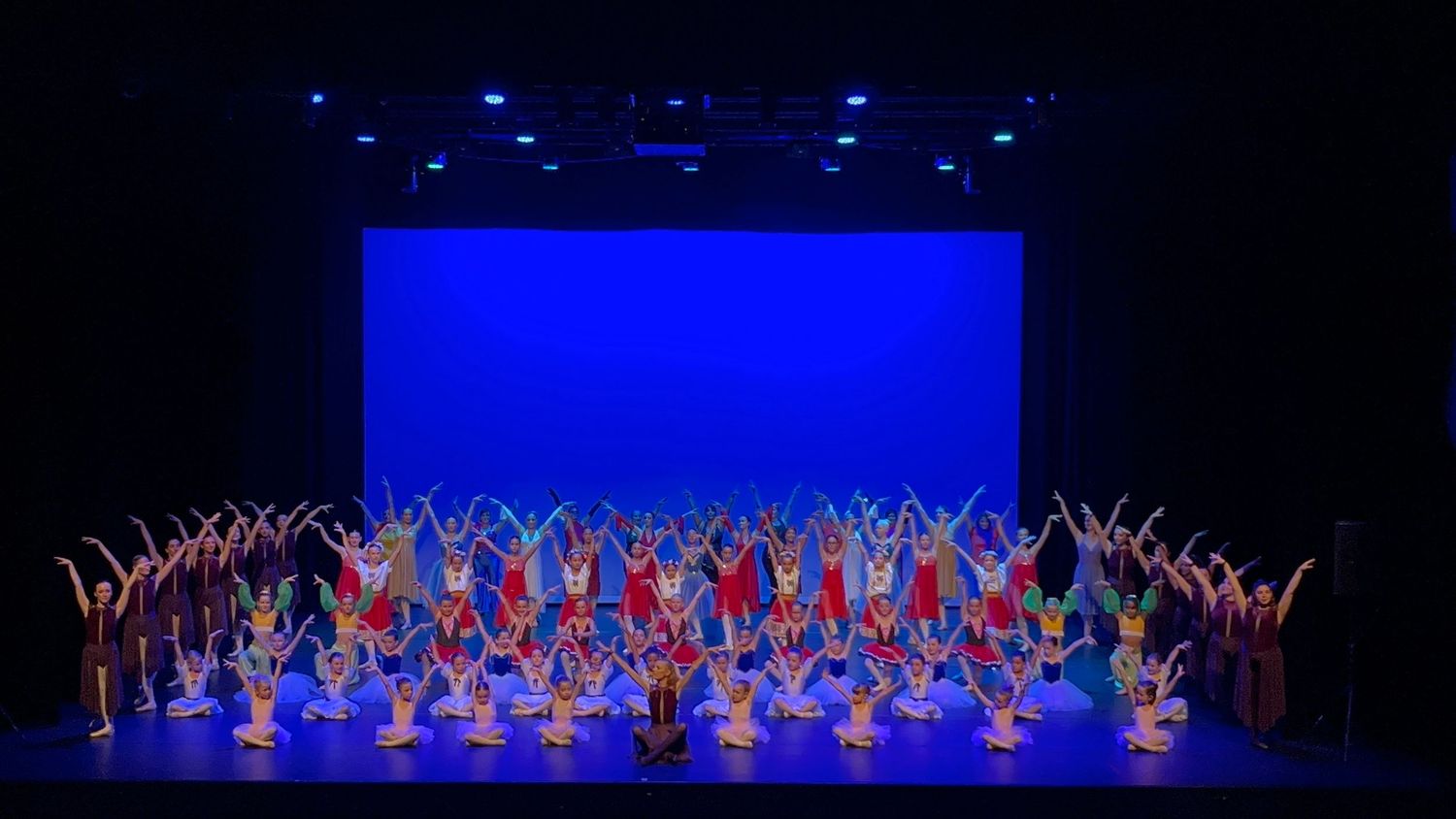 Large dance performance with blue lighting on stage showing synchronized dancers.