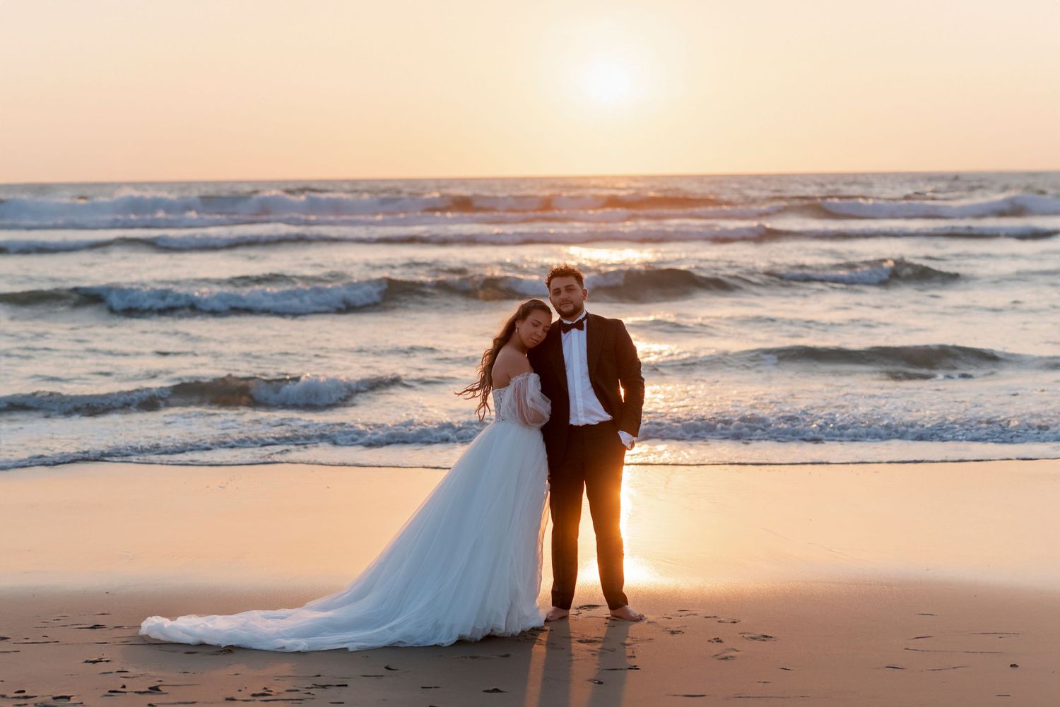 Romantic beach wedding photoshoot at sunset with waves crashing in the background.