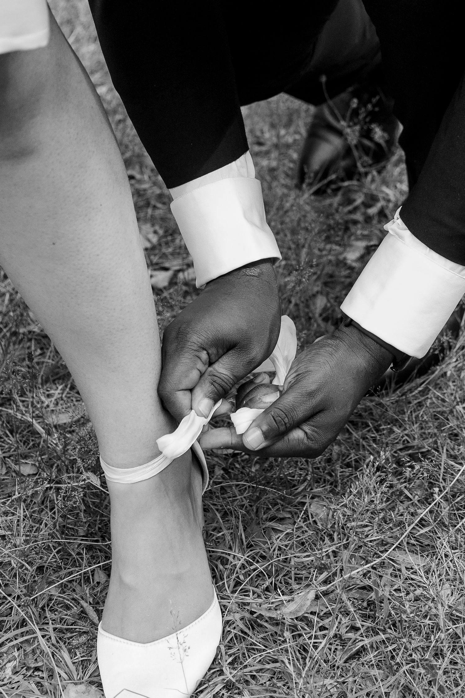 Black and white photo of wedding shoe being fastened on grass.