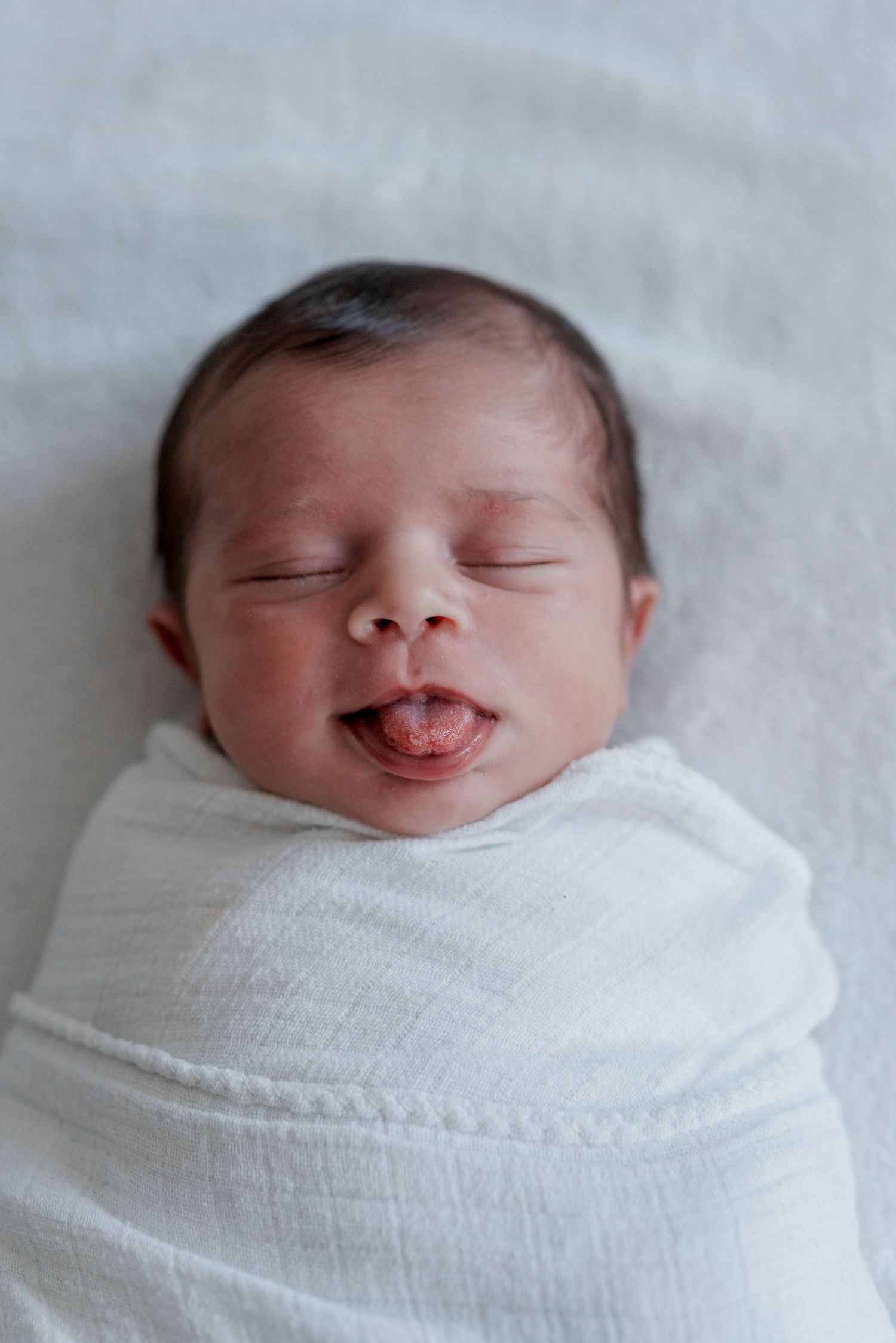 Newborn baby wrapped in white swaddle smiling with closed eyes.