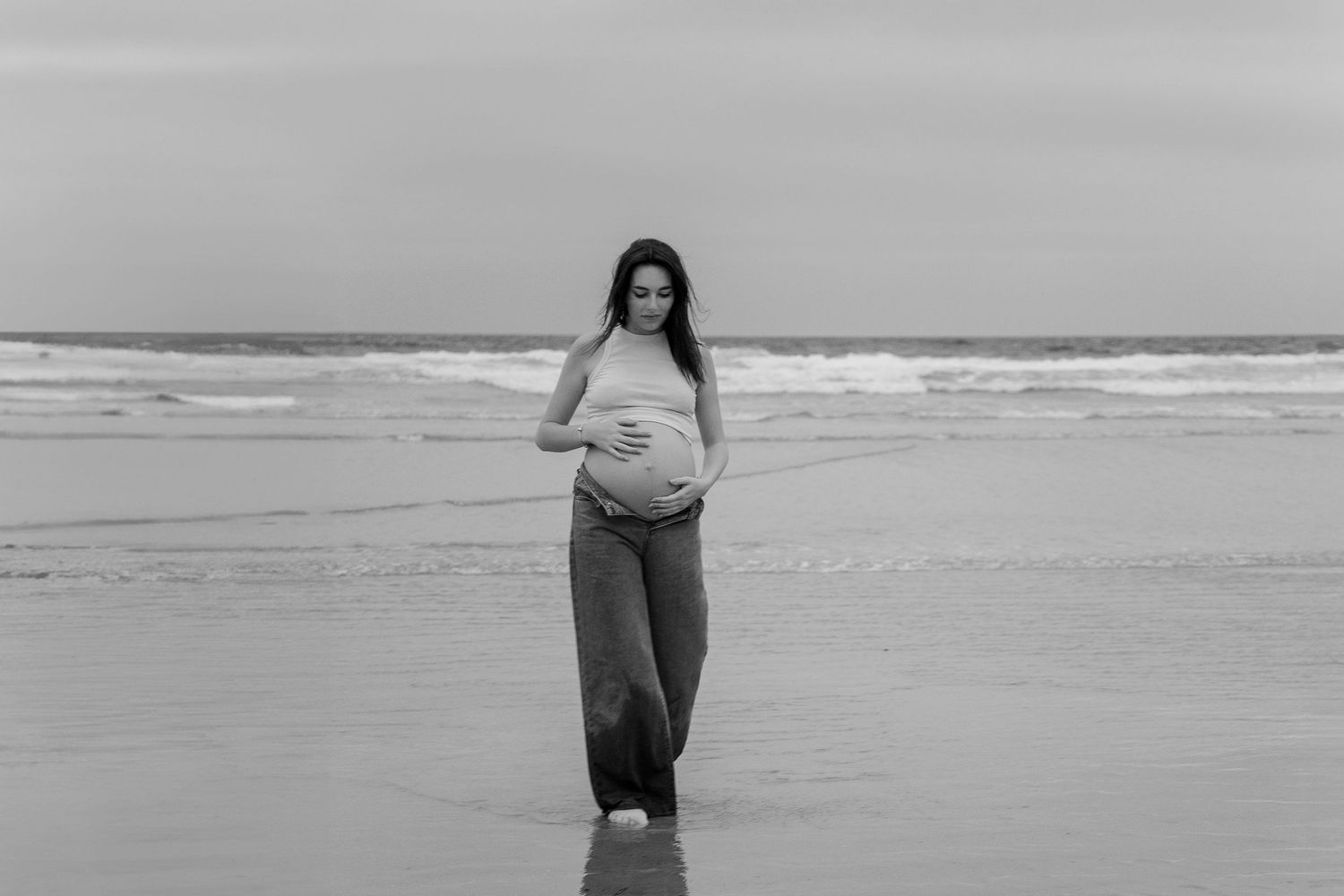 A person walks along a misty beach shoreline in black and white.