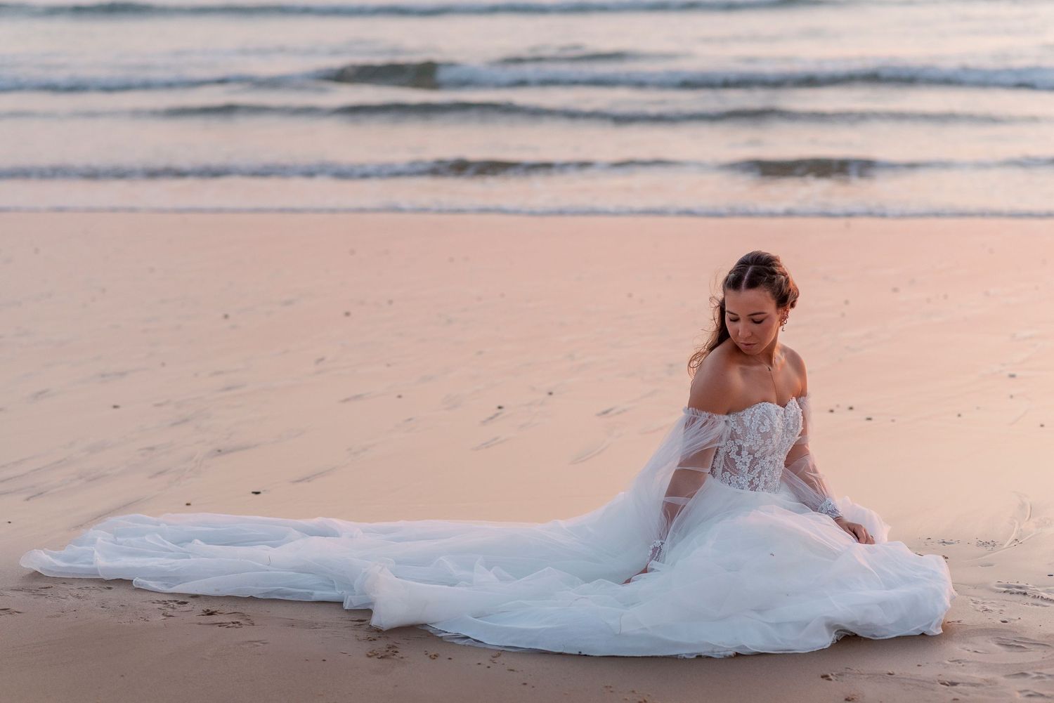 Wedding dress flowing across sandy beach at sunset.