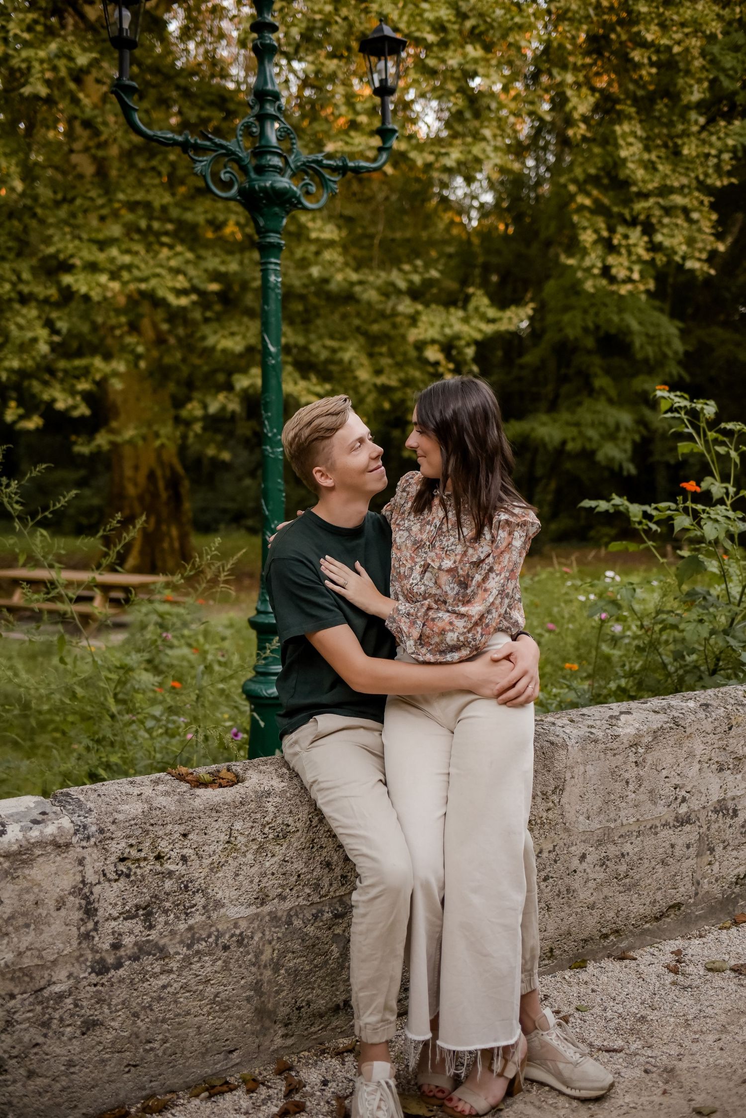 Couple sharing intimate moment while sitting on stone wall surrounded by autumn foliage.