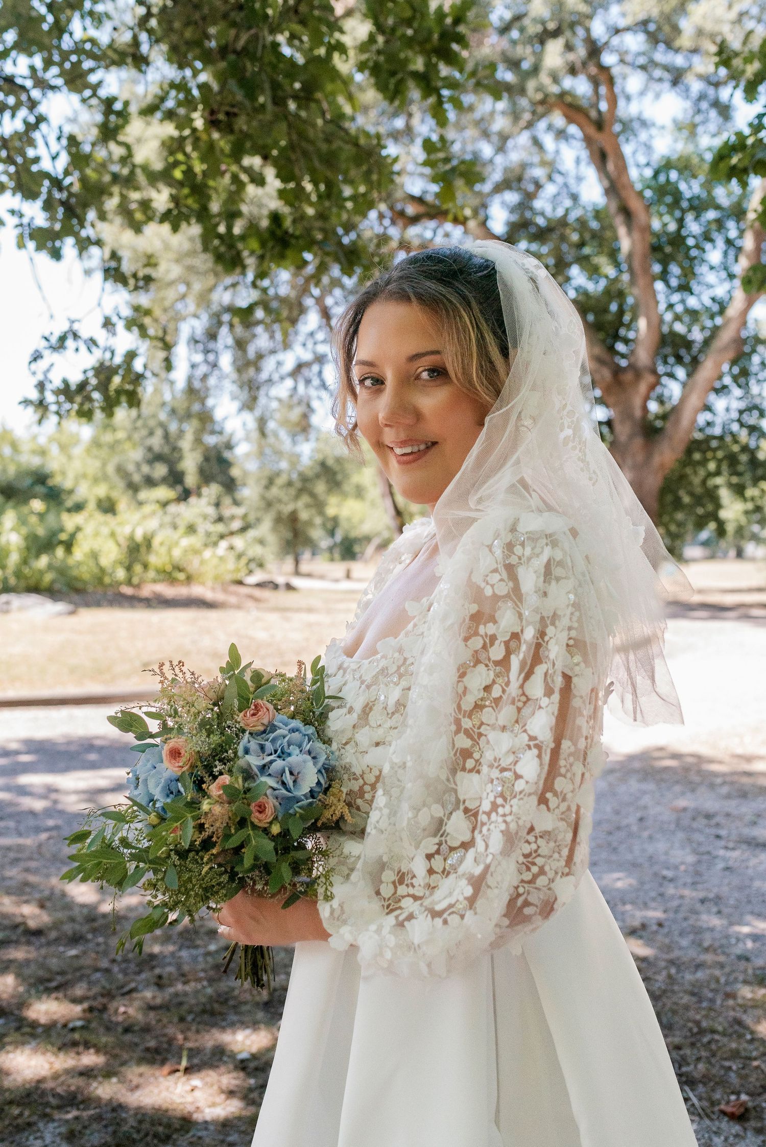 Bride holding delicate bouquet with blue and peach flowers against lace details.