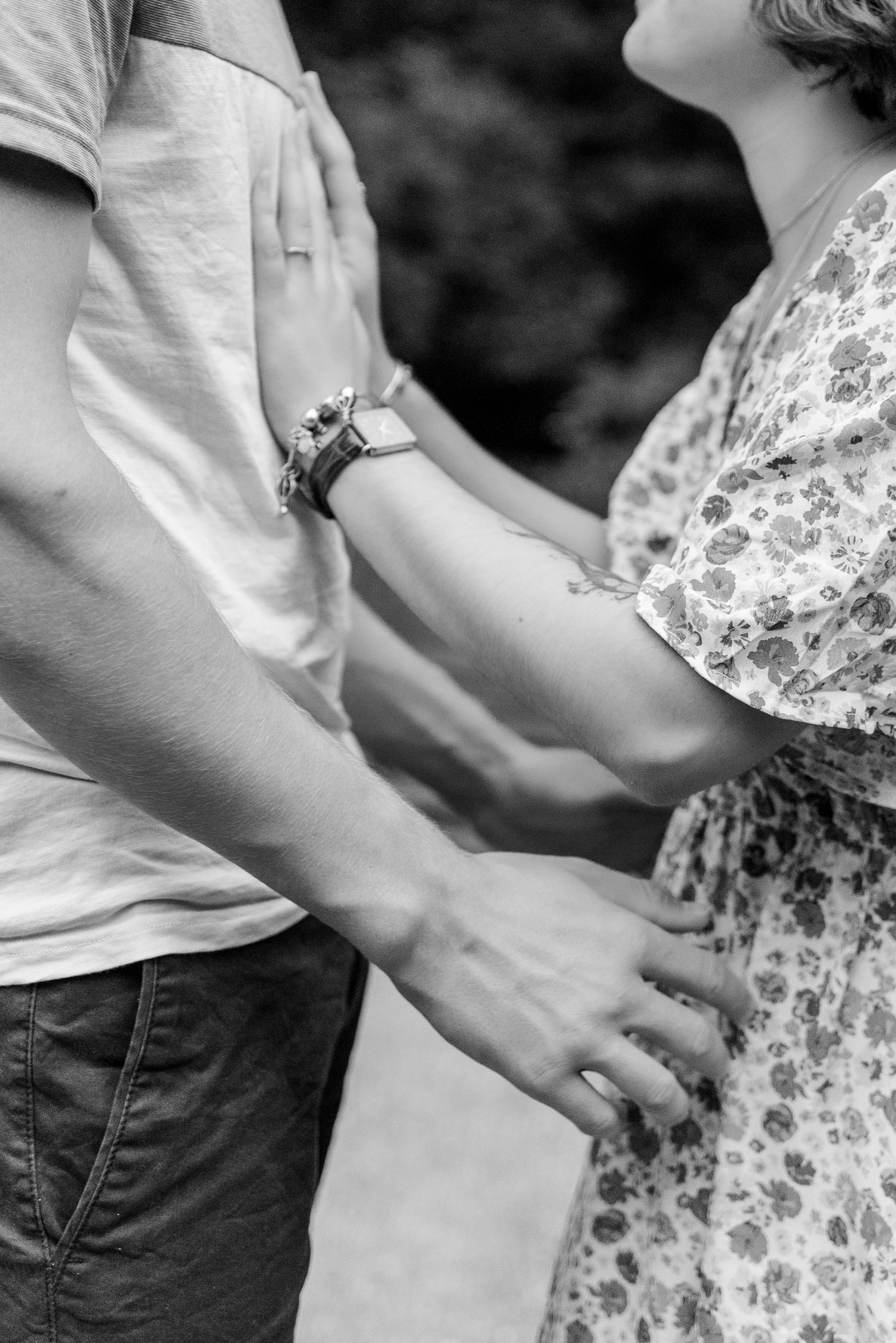 Close-up black and white shot of couple's tender embrace showing hands and floral dress detail.