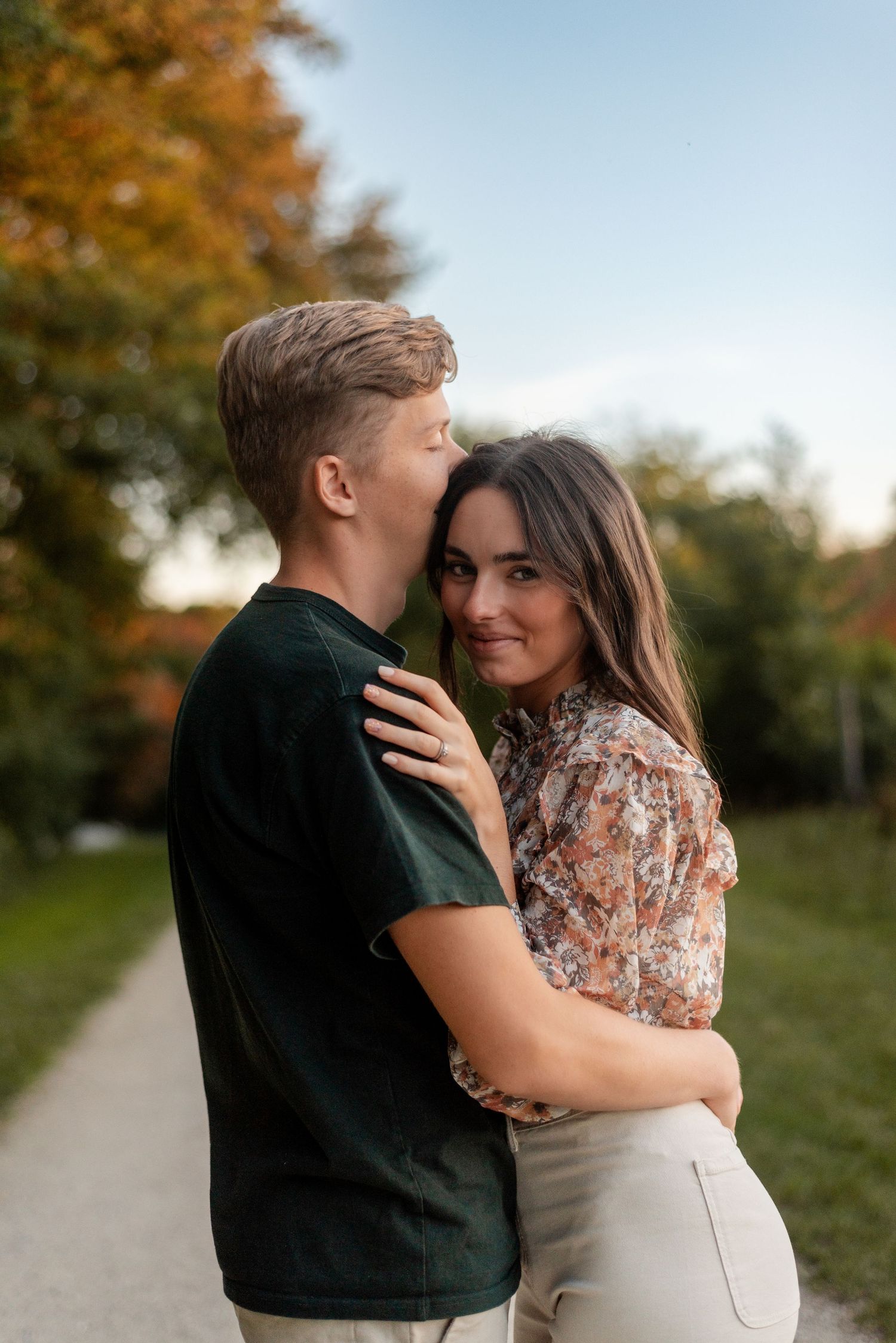 Romantic couple embracing on path with fall colors and natural lighting.
