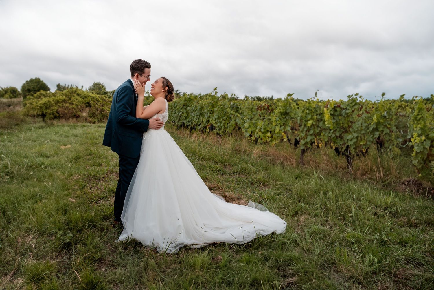 Romantic wedding couple embracing in a vineyard under cloudy skies.