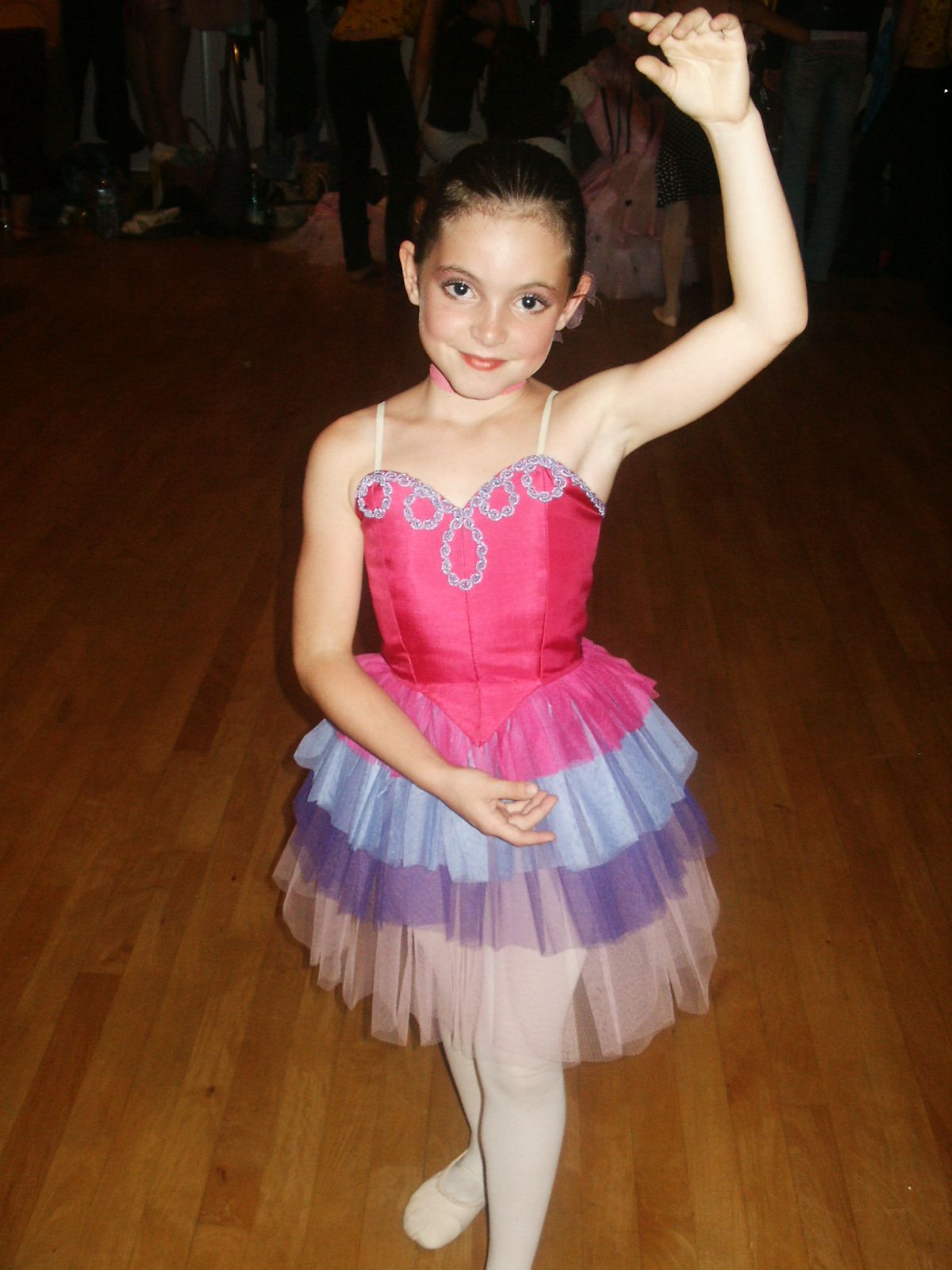 Young dancer in pink and purple tutu dress performs gracefully on wooden floor.