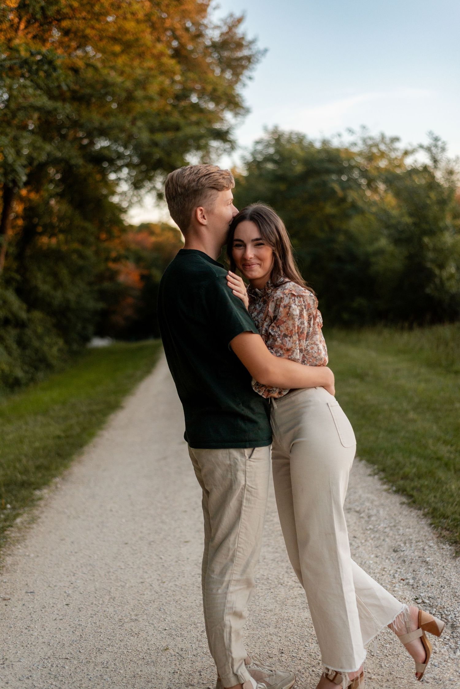 Couple embracing on gravel path during golden hour engagement session.