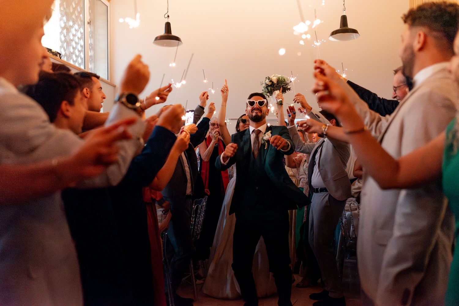 Wedding reception celebration with guests holding sparklers in warm evening light.