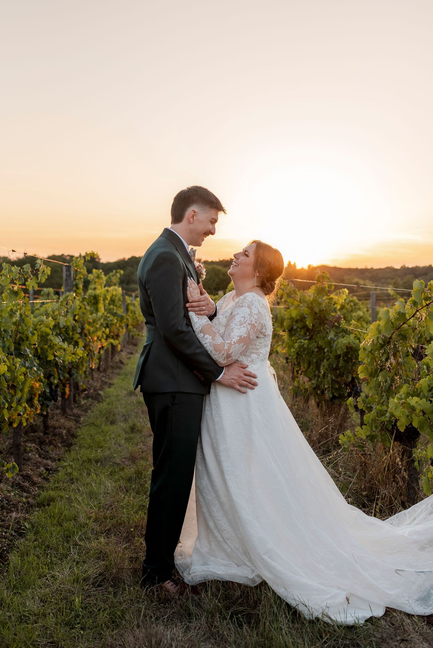Romantic wedding couple dancing and embracing in a vineyard during golden hour.