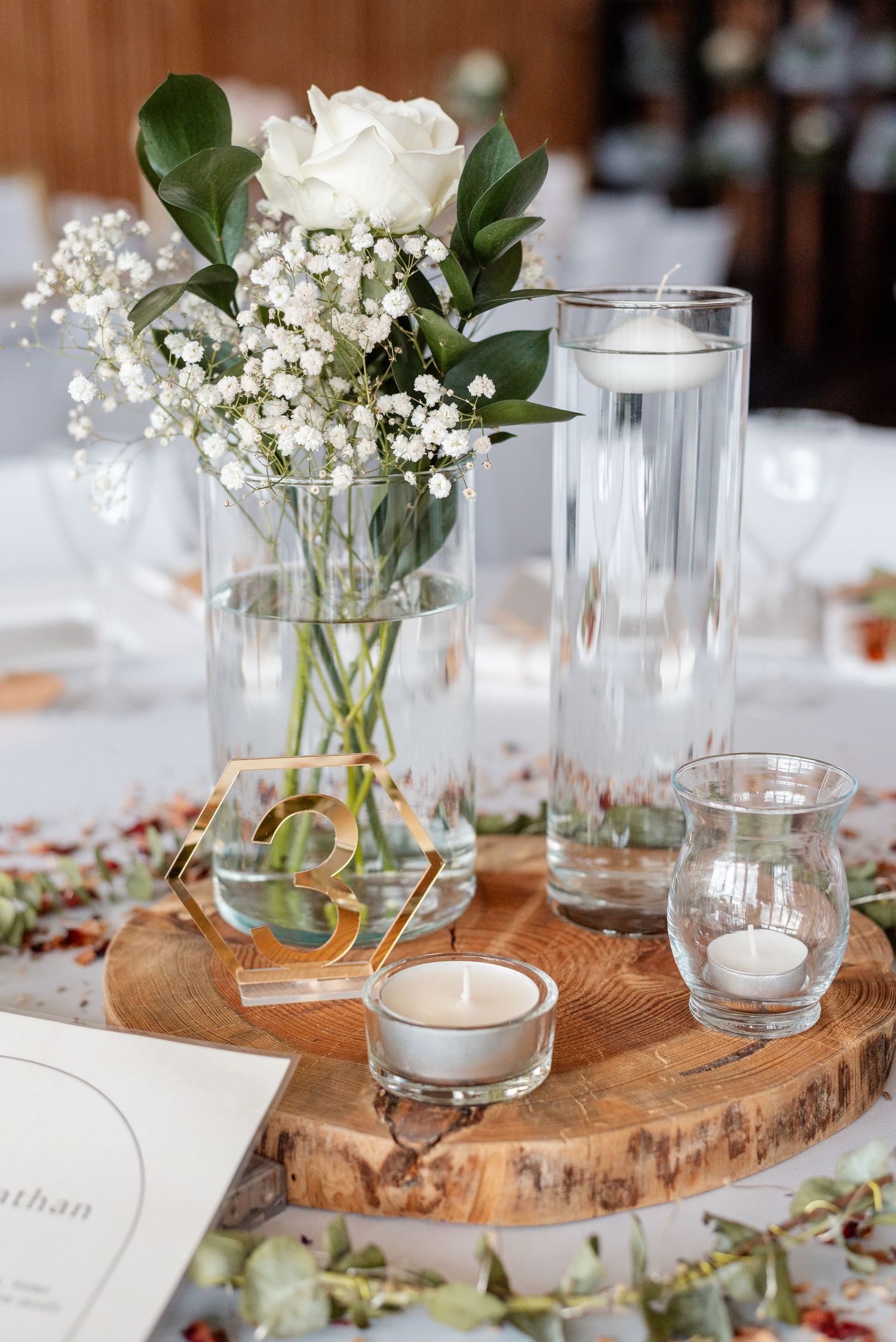 Elegant wedding centerpiece with white roses and baby's breath on a rustic wood slice with candle votives.