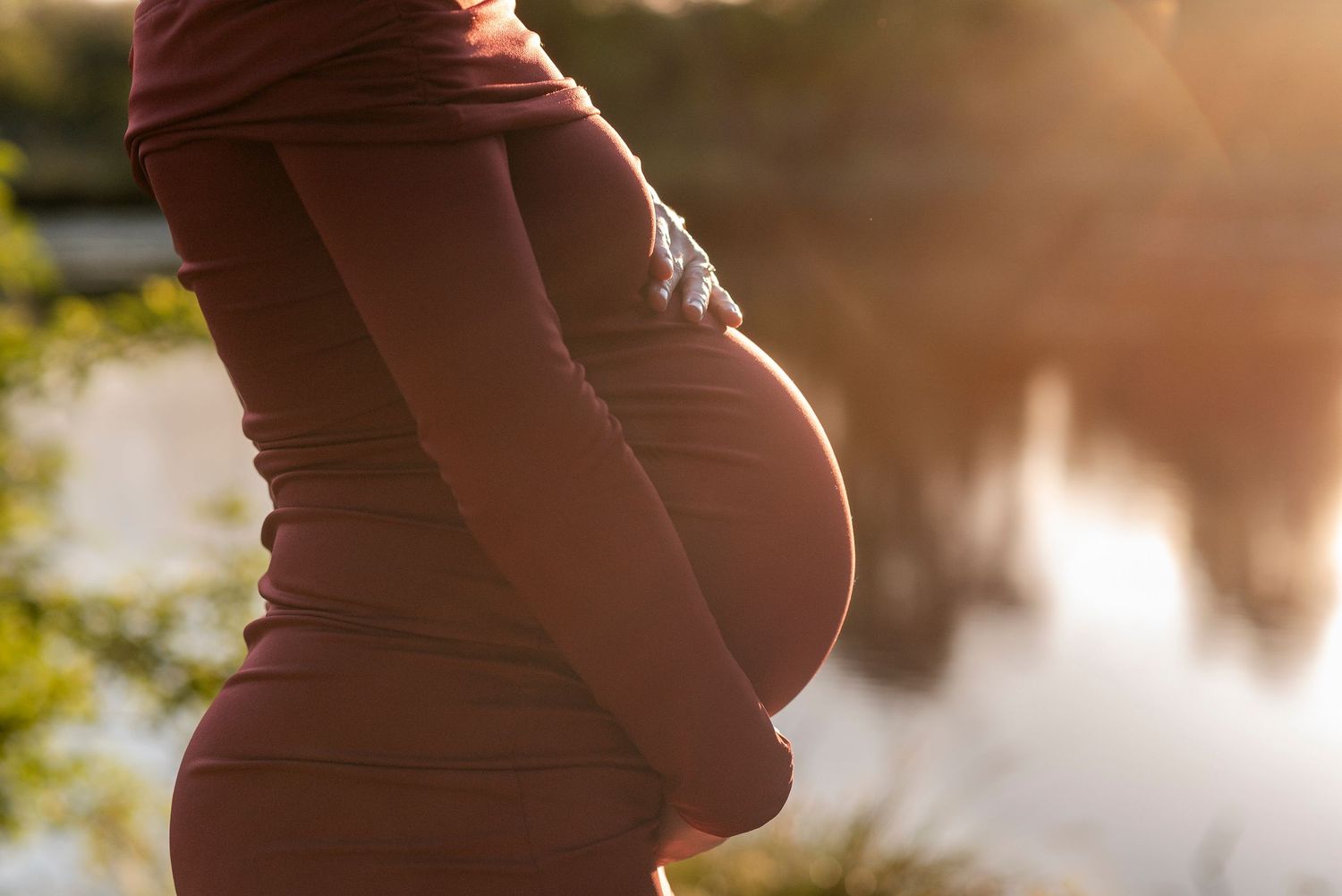 Silhouette of a pregnant belly against a golden sunset backdrop.